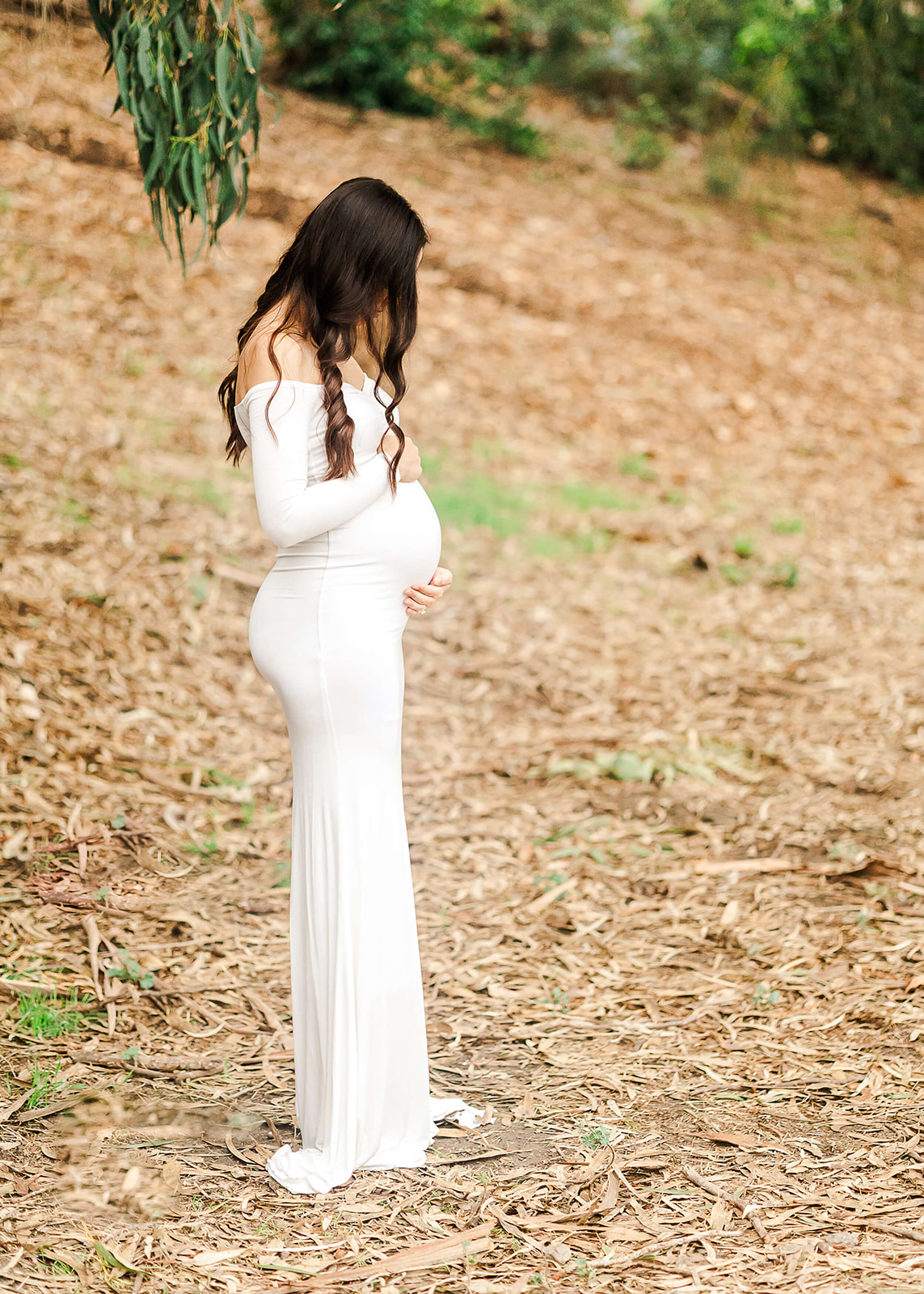 pregnant woman in white gown cradling her bump and looking at it