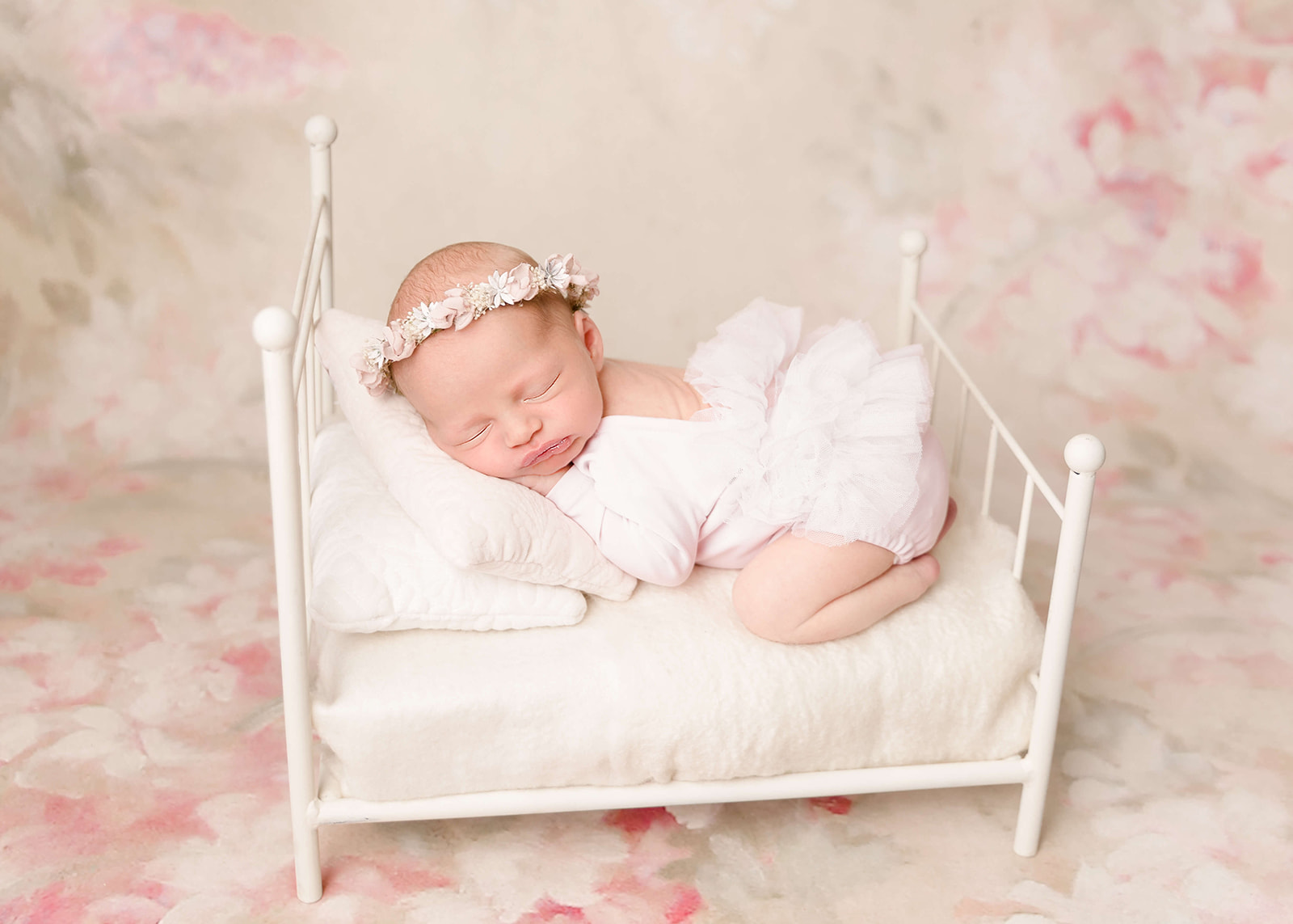 A newborn baby girl sleeps on a tiny white bed surrounded by flowers while wearing a floral headband and a pink tutu Los Angeles Birthing Centers