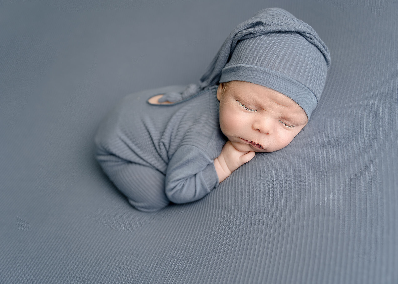 A newborn baby sleep in a blue onesie and matching night cap Los Angeles Doulas