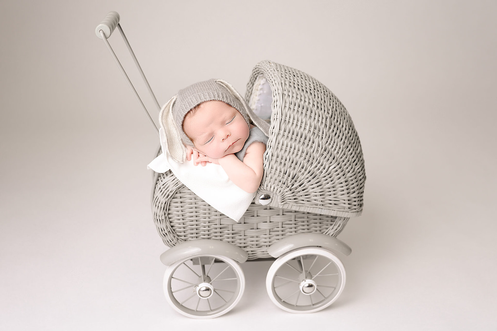 A newborn baby sleeps in a tiny wicker baby carriage in a grey onesie and hat Los Angeles Doulas