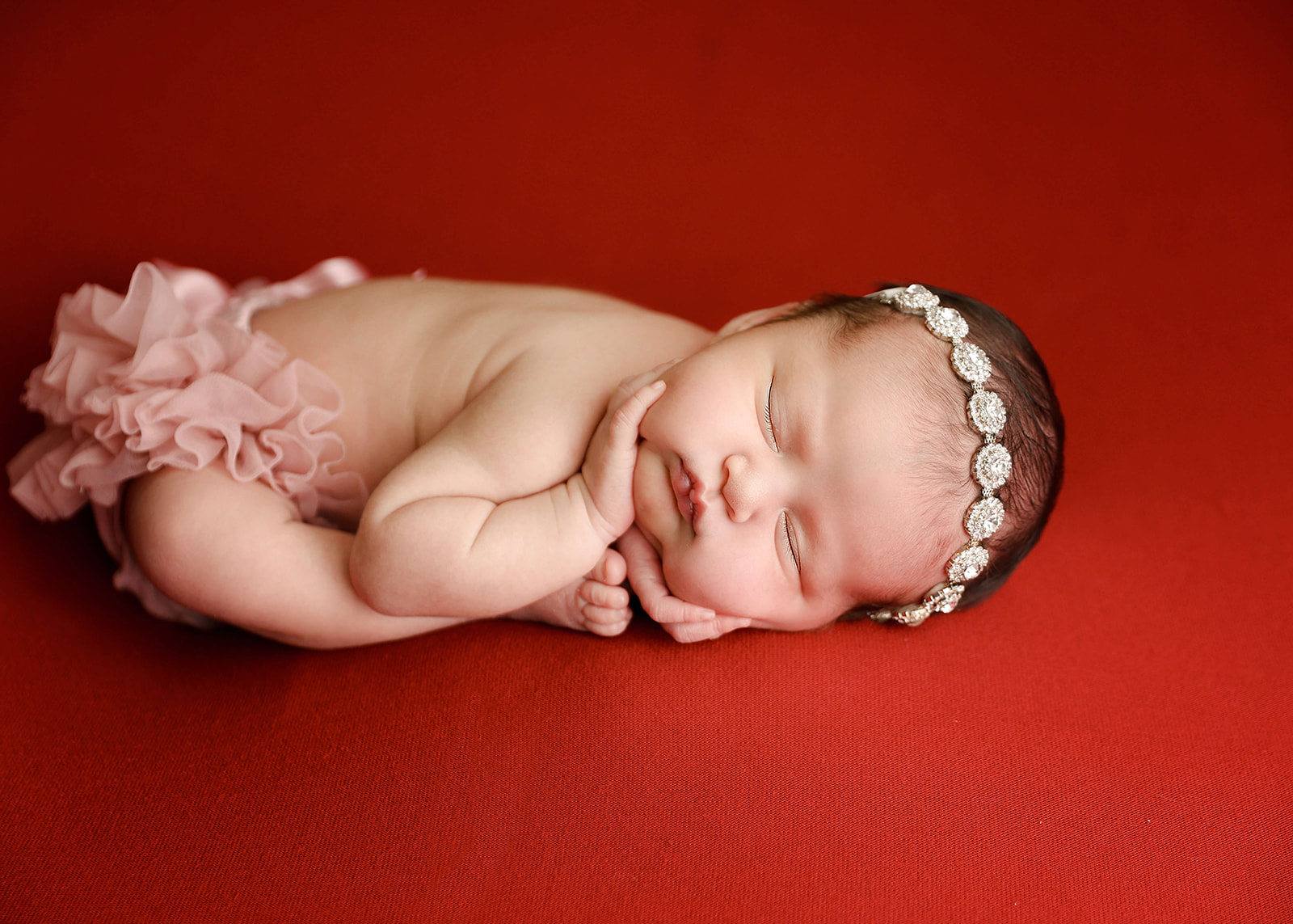 A newborn baby sleeps on a red bed with hands on her face wearing a pink tu tu Los Angeles Midwives
