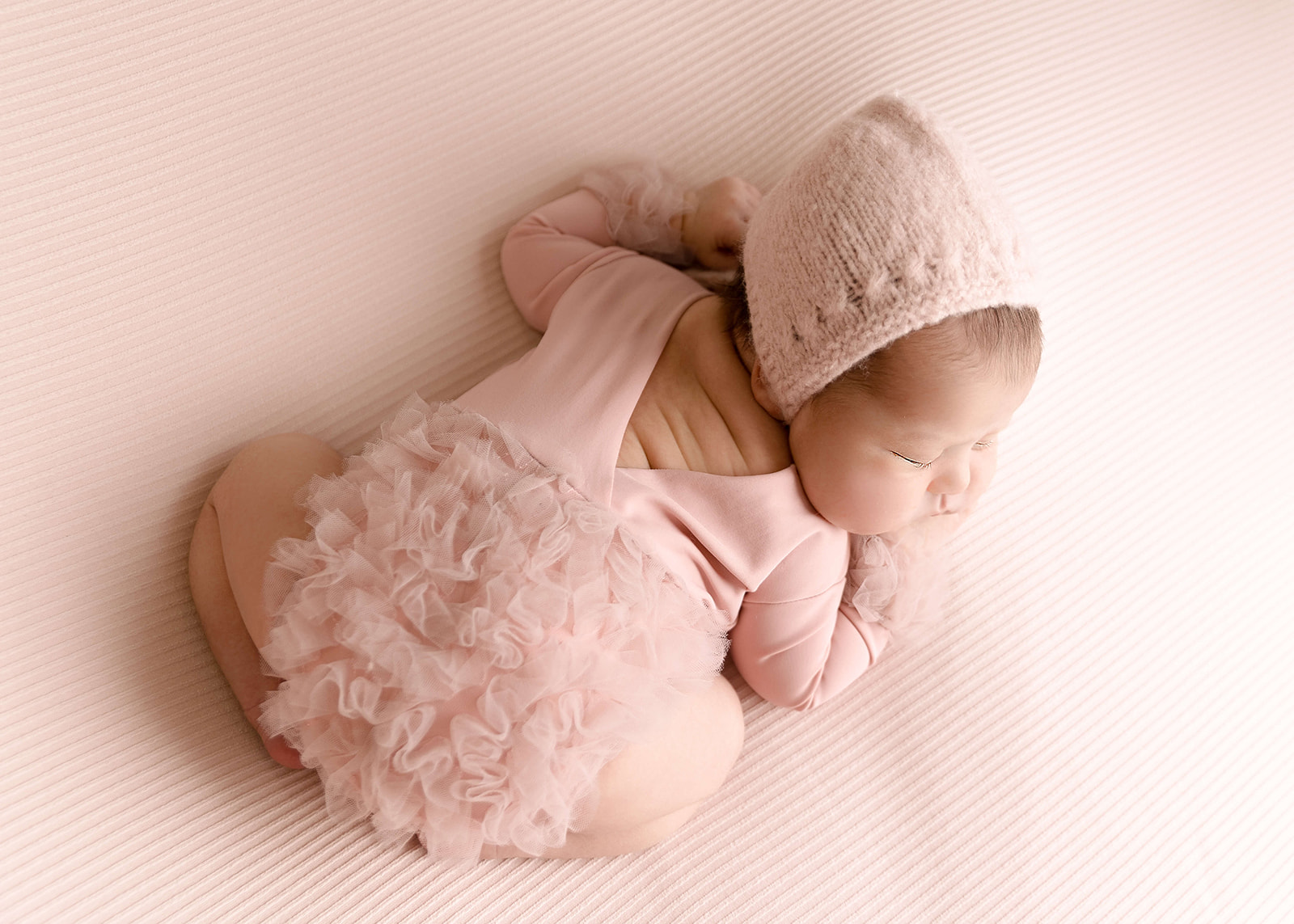 A newborn baby sleep in a froggy pose whiile wearing a pink tule onesie Los Angeles Midwives