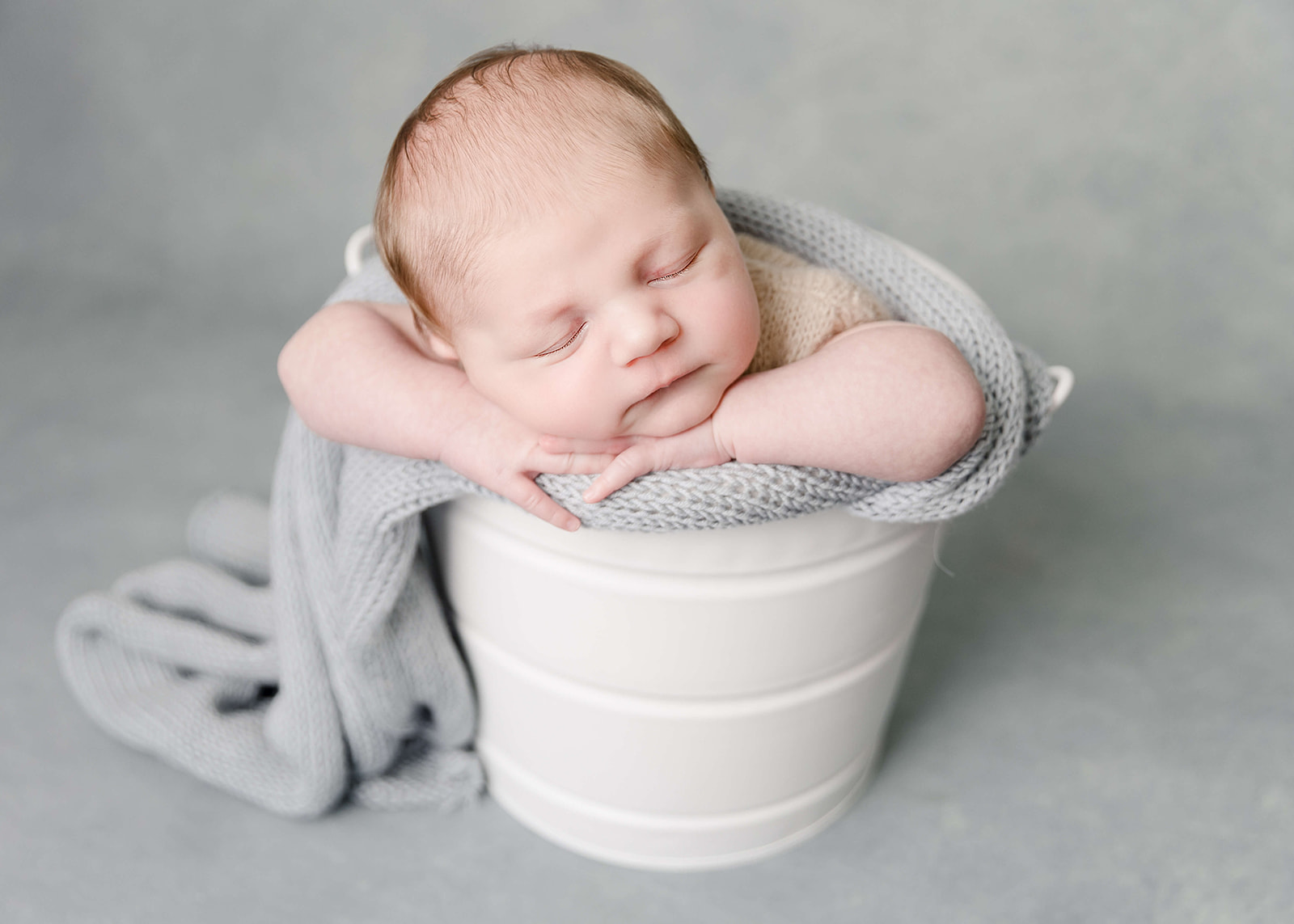 A newborn baby sleeps in a bucket wrapped in a blue blanket with head resting on its hands Irvine Pediatrician