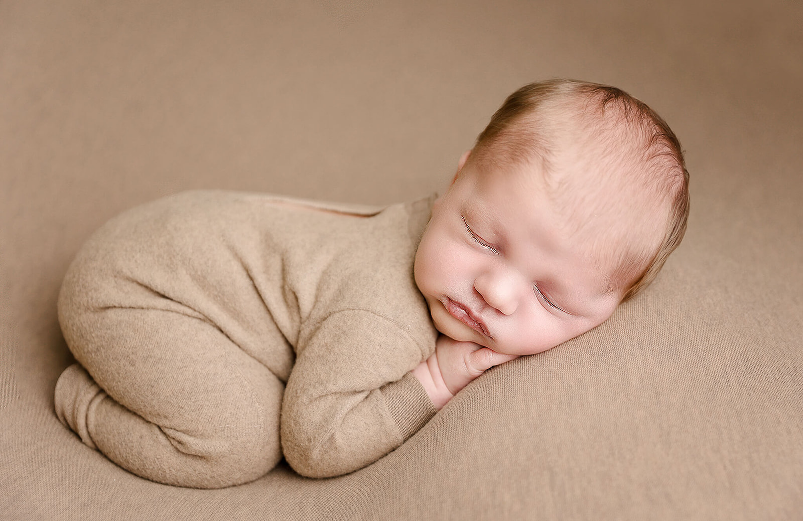 A newborn baby sleeps on a soft brown bed in a froggy pose Irvine Pediatrician