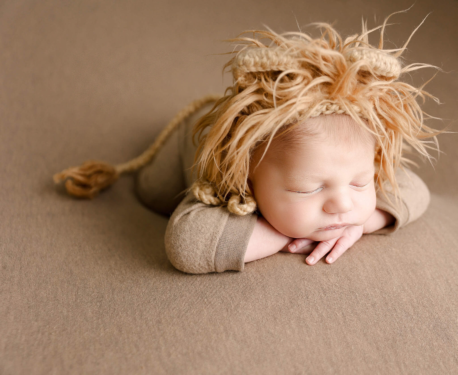 A newborn baby wearing a lion hat with a tail sleeps on a brown bed Irvine Pediatrician
