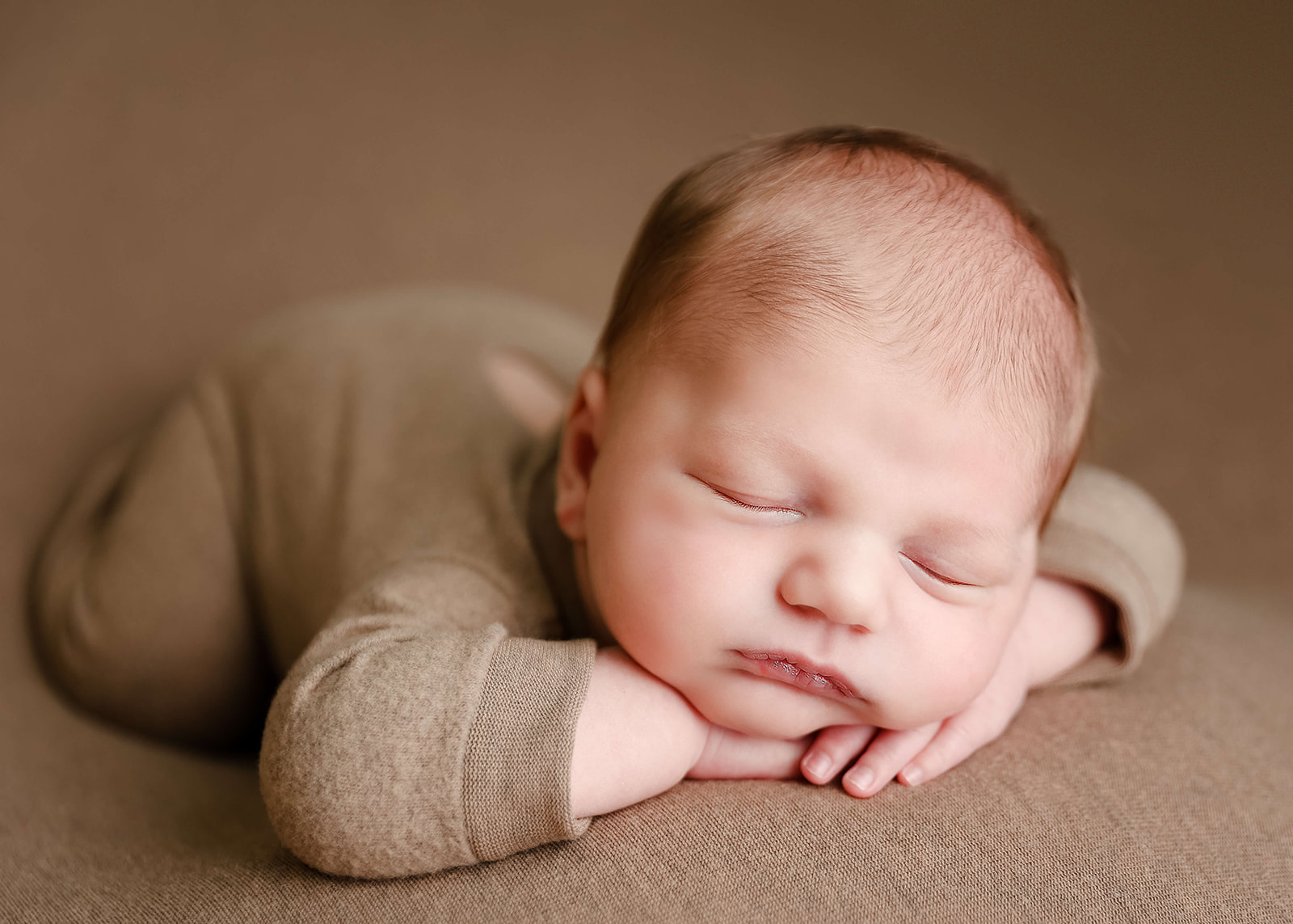 A newborn baby sleeps in a brown onesie with its head resting on its hands Irvine Pediatrician