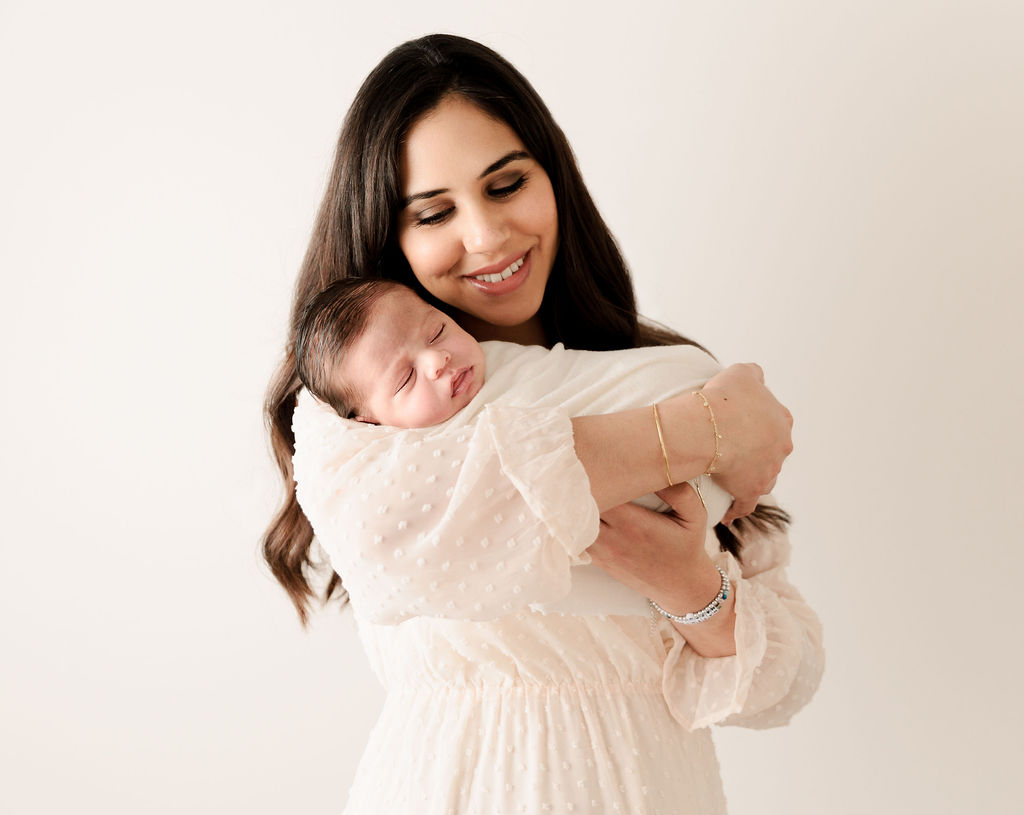 A mother holds her newborn baby while it sleeps in a white swaddle neiman marcus newport beach