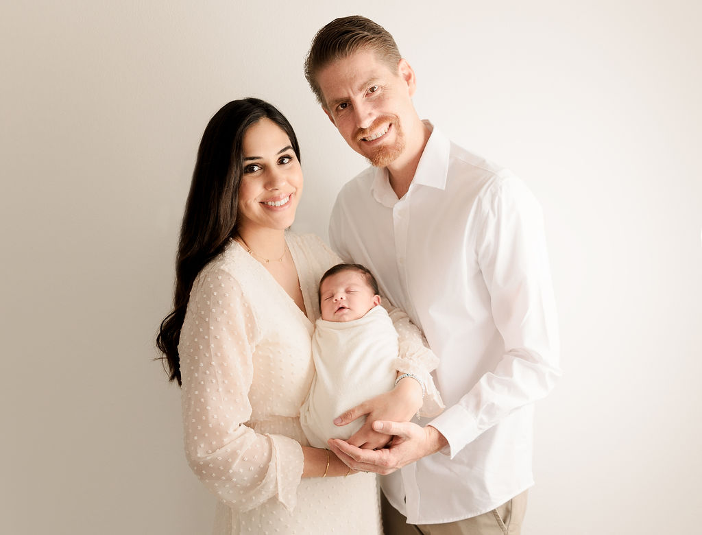 New parents stand in a studio holding their newborn baby