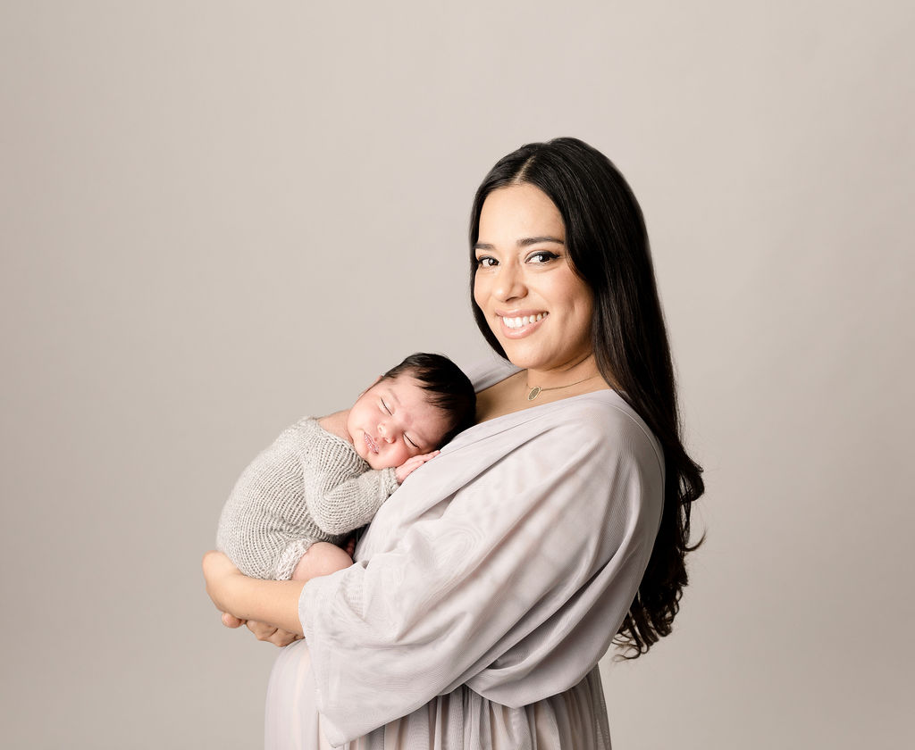 A mother in a grey dress holds her newborn baby on her chest newport beach pediatricians