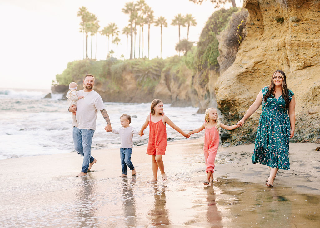 A family of six hold hands and walk down a beach things to do in newport beach with kids