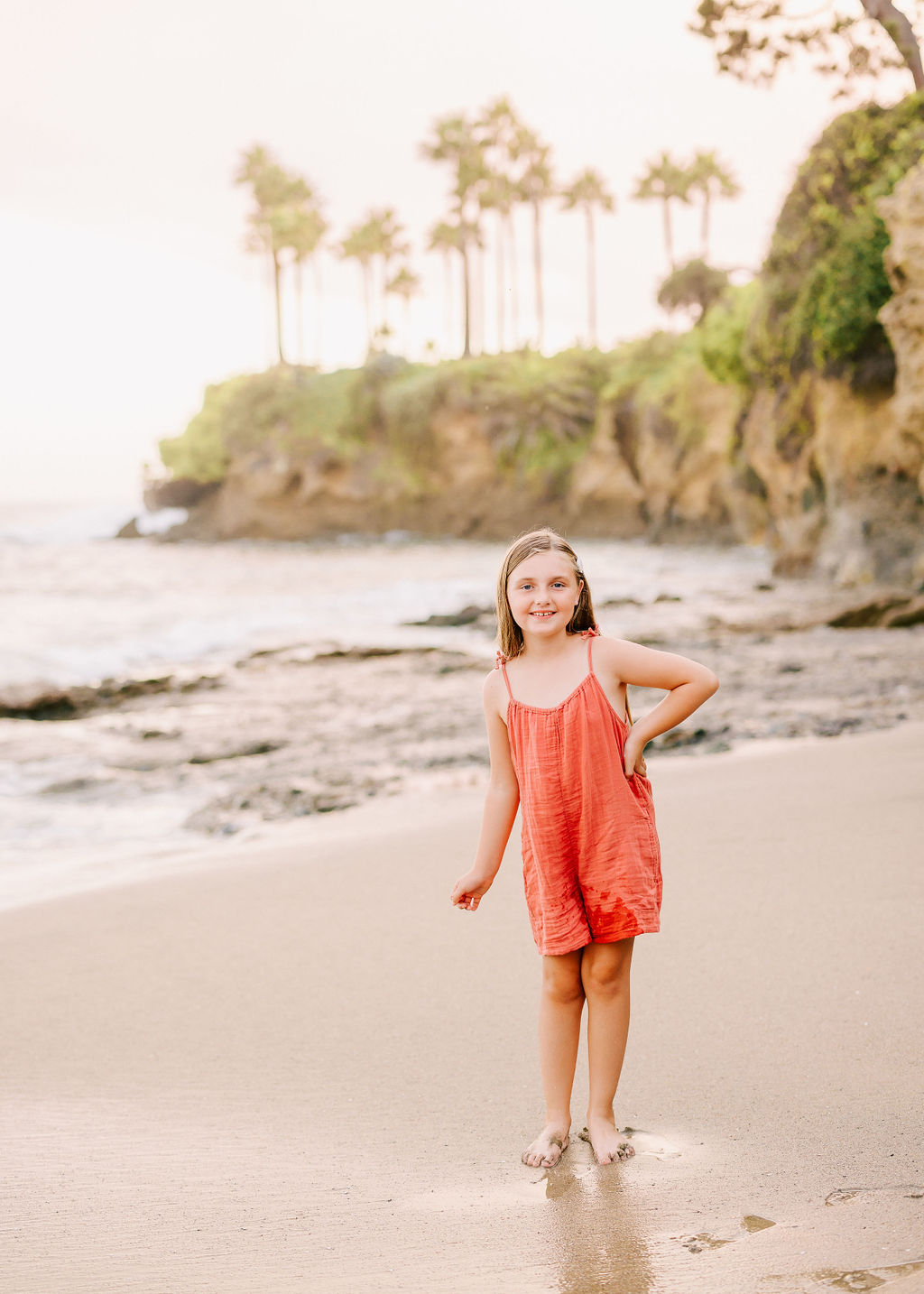 A young girl stands in wet sand on a beach with a hand on her hip things to do in newport beach with kids