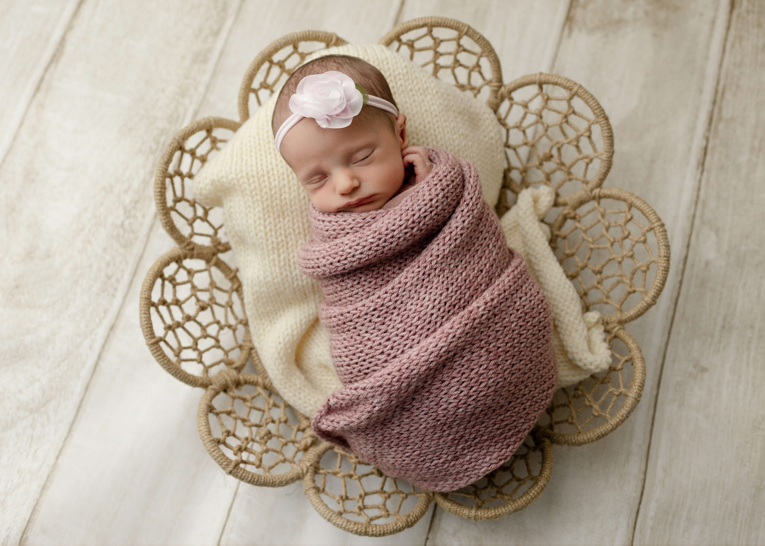 Baby girl posed in boho basket on wood floor.
