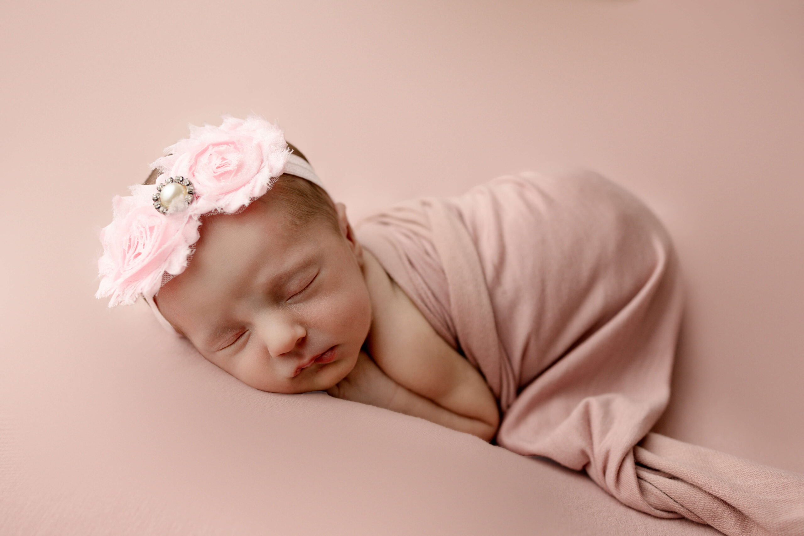 Baby wrapped on bean bag sleeping with a flower headband.