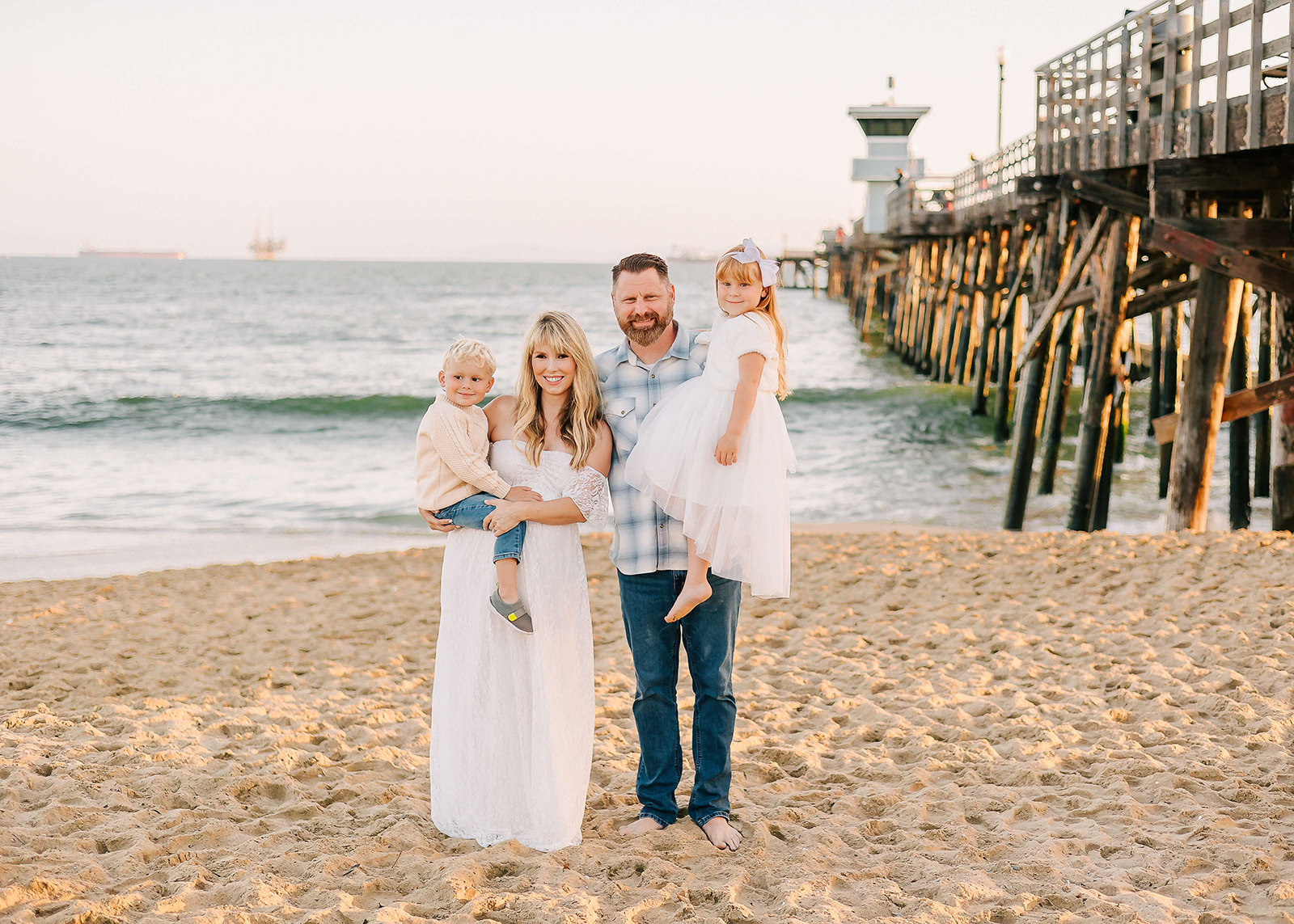 A family of four stand on the beach next to the pier at sunrise Los Angeles Pediatricians
