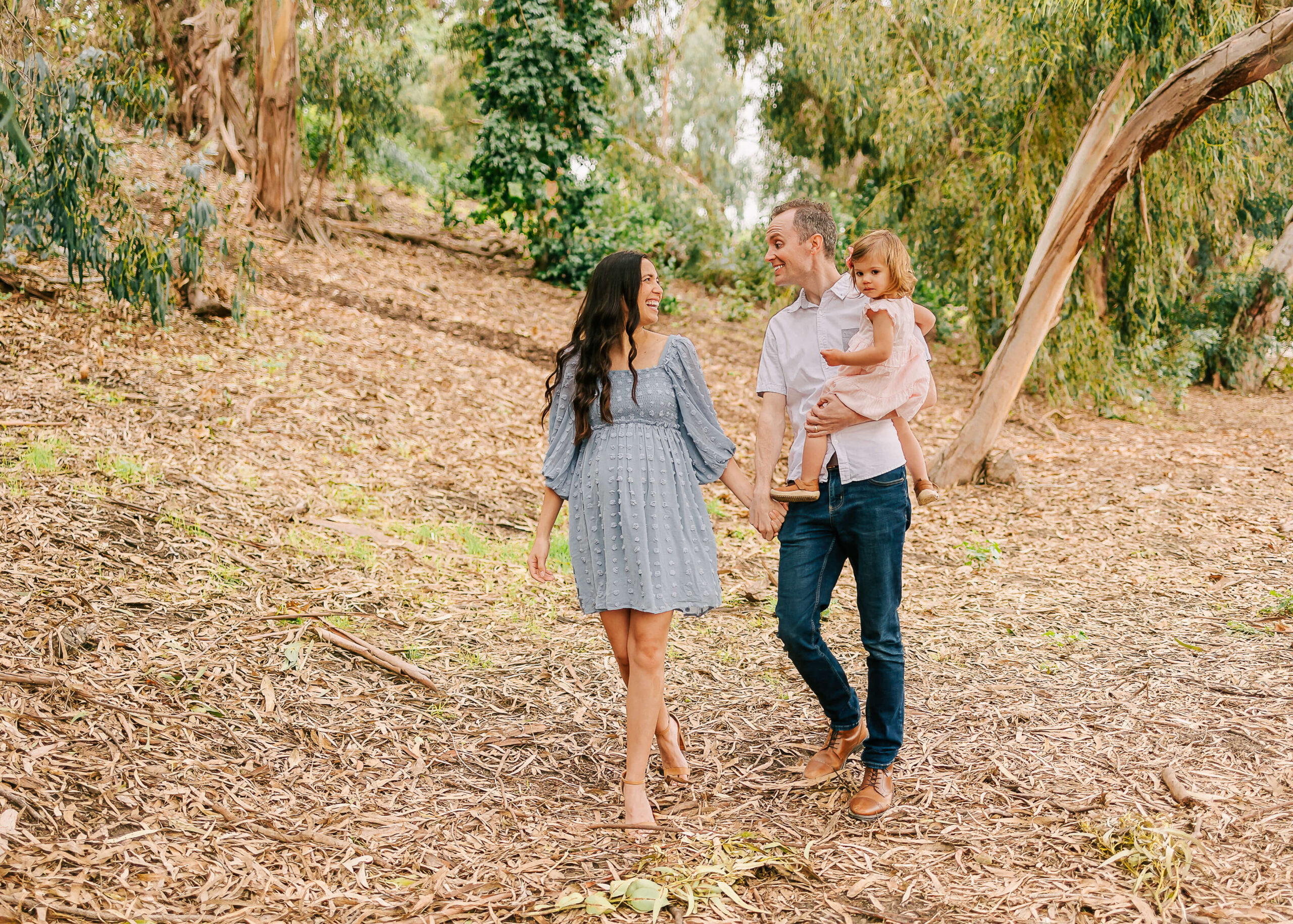 Family walking holding hands, dad is holding the big sister at nature maternity session in Los Angeles. By Ashley Nicole Photography.