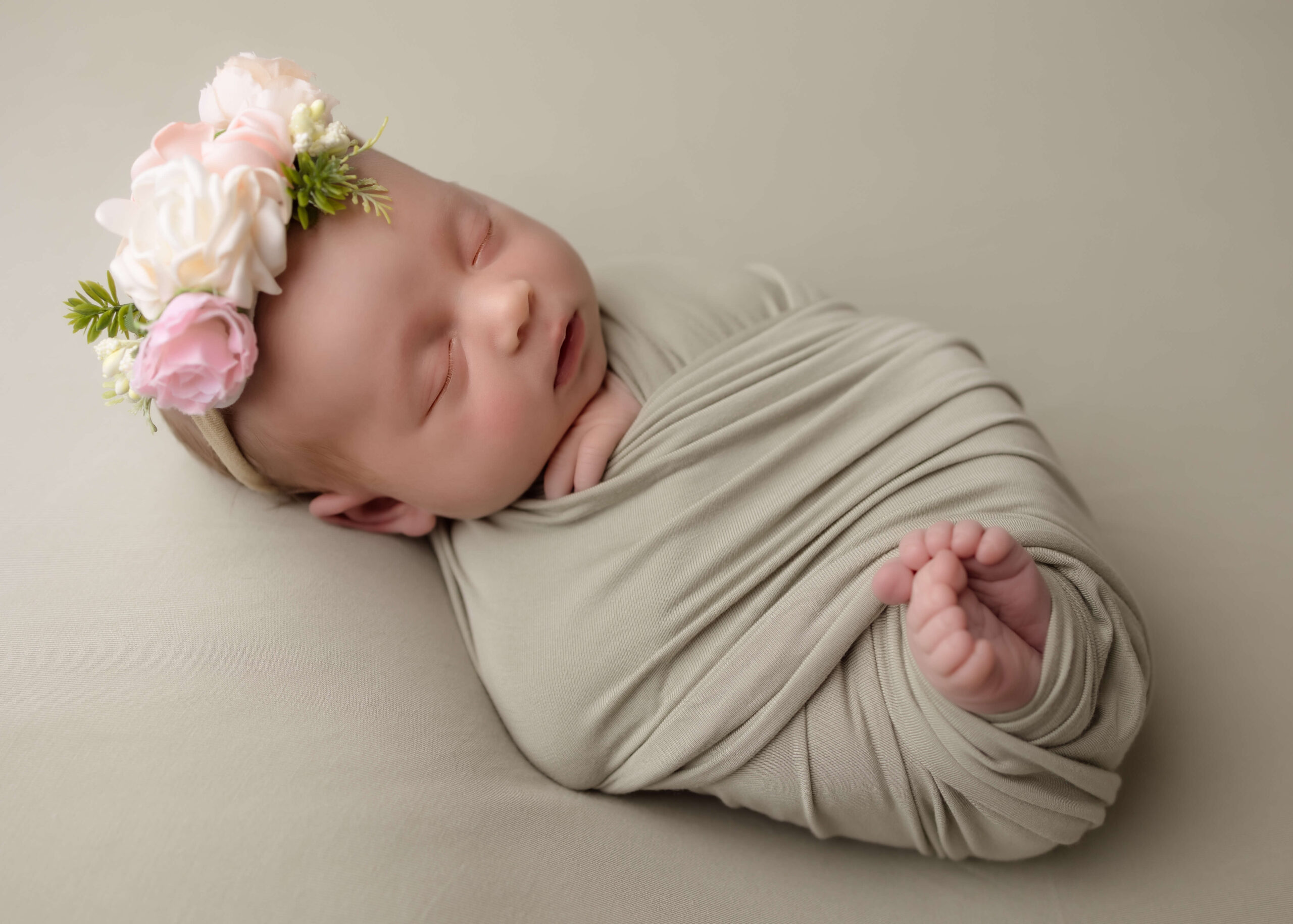 Baby girl swaddled and wearing flower headband while sleeping.