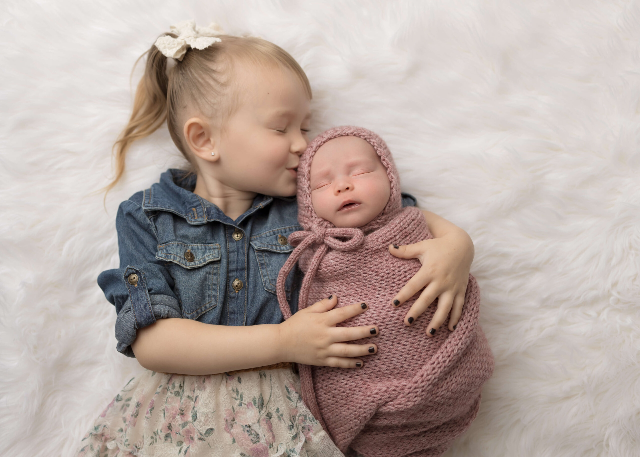Big sister kissing her new baby sister while in studio newborn session by Ashley Nicole Photography.