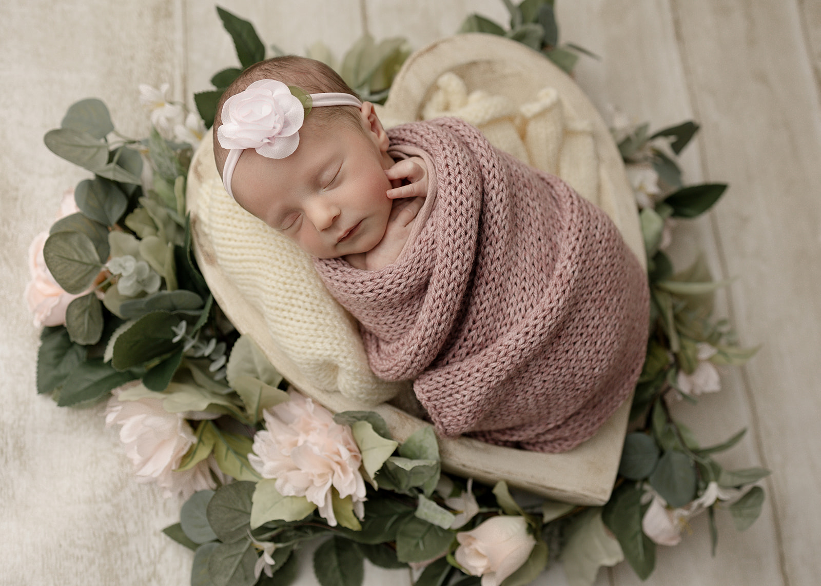 A newborn baby sleeps on a bed of roses in a heart-shaped bowl and pink knit swaddle Huntington Beach Pediatricians