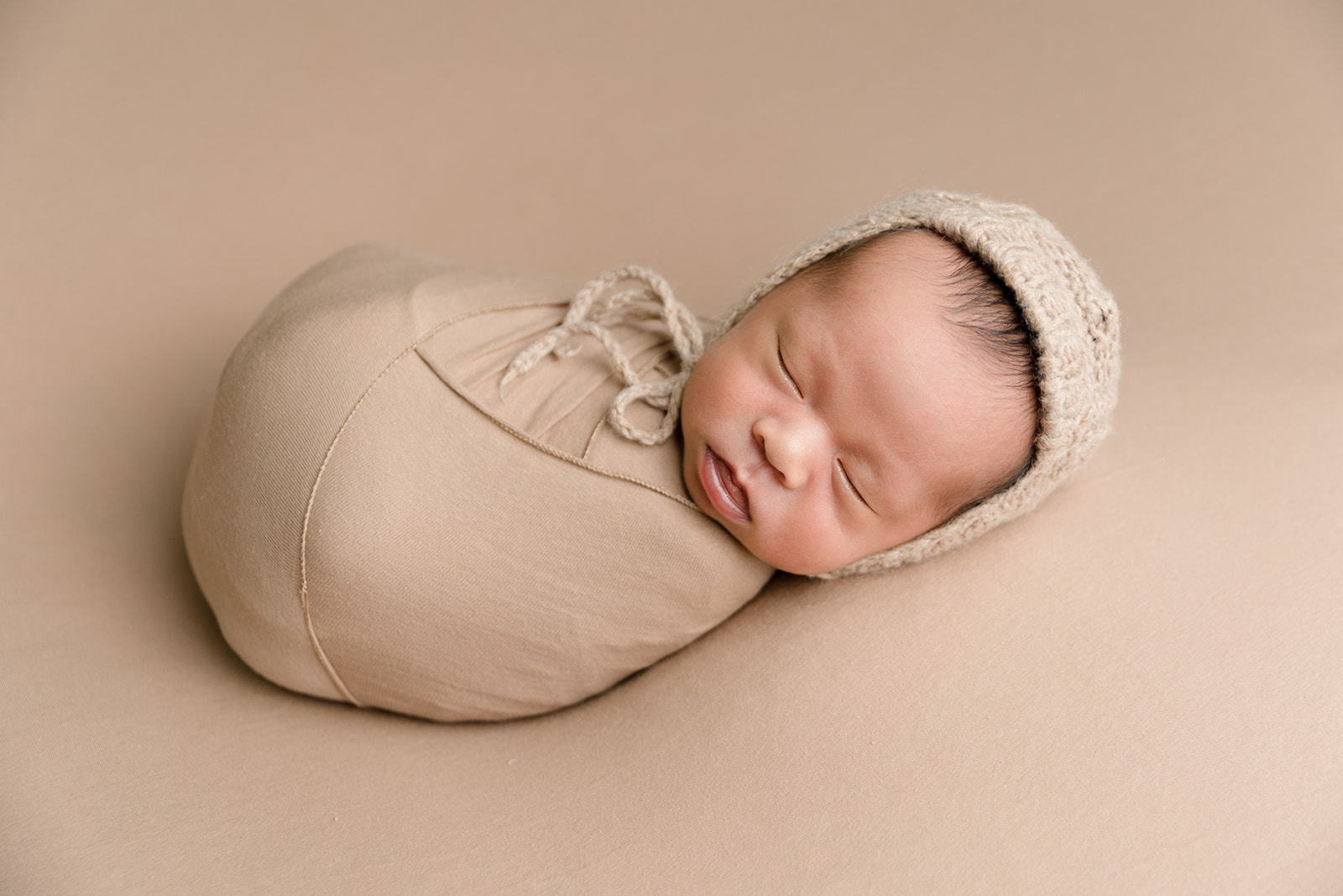 A newborn baby sleeps in a brown onesie
