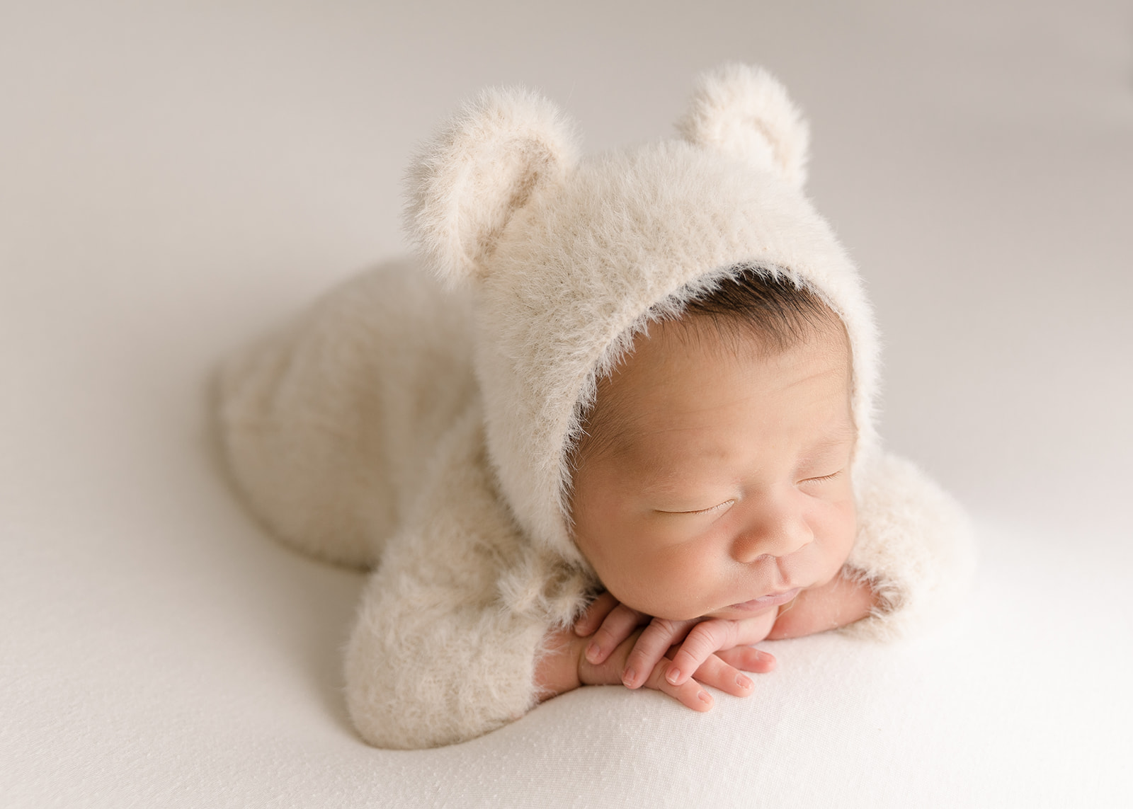A newborn baby sleeps in a white furry onesie and bonnet with ears Irvine Midwife