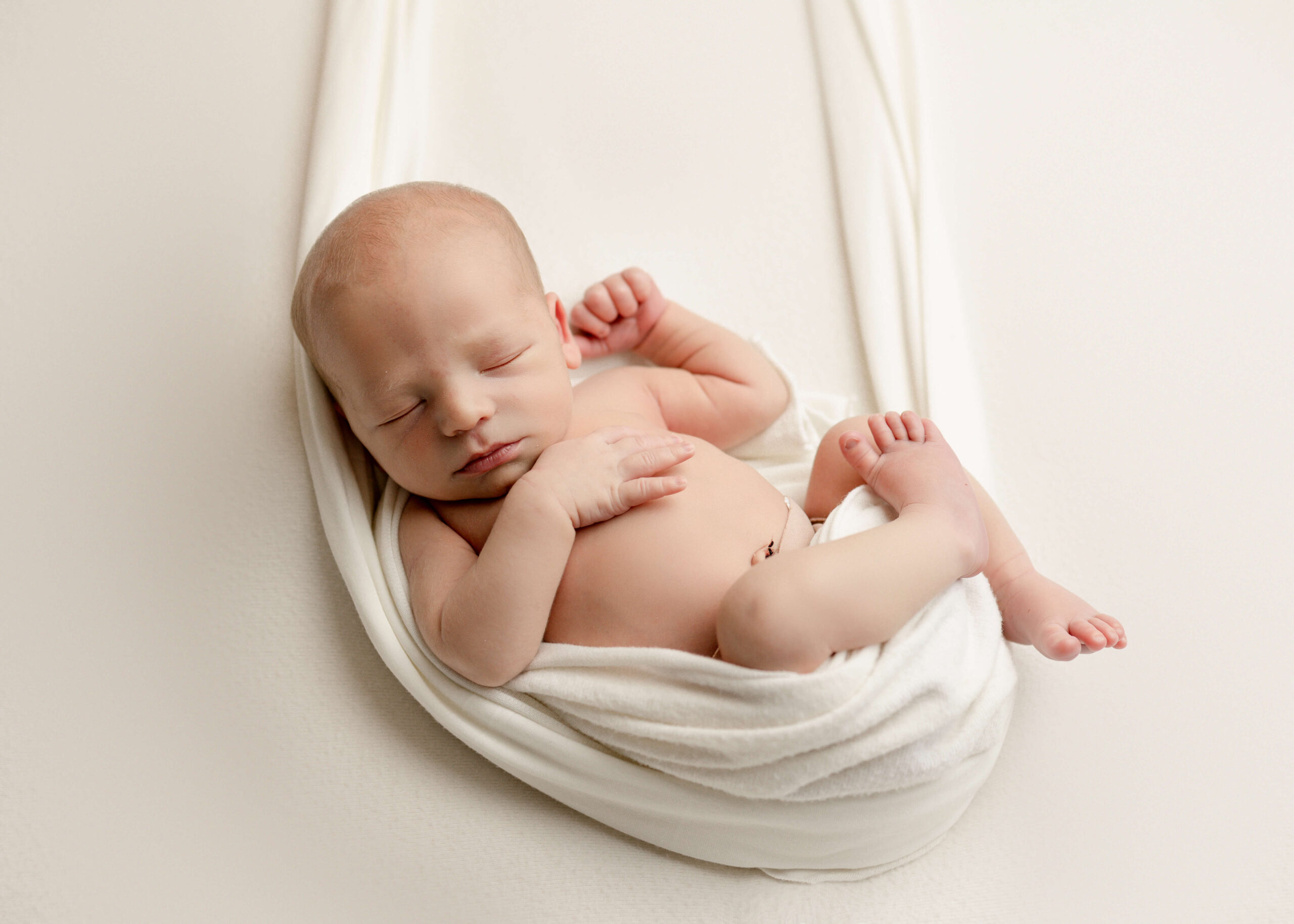 Newborn baby boy posed in swing in studio session by Ashley Nicole.
