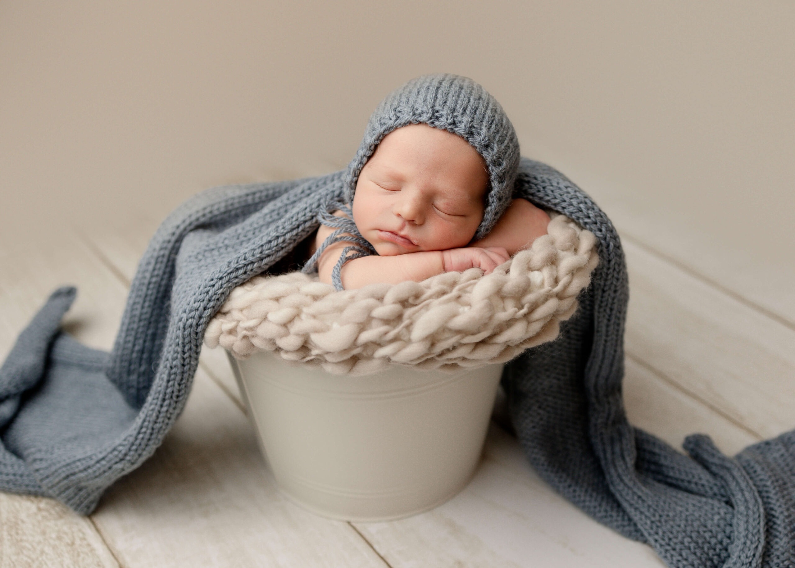 Newborn baby posed with blue knit bonnet in bucket in studio session by Ashley Nicole.