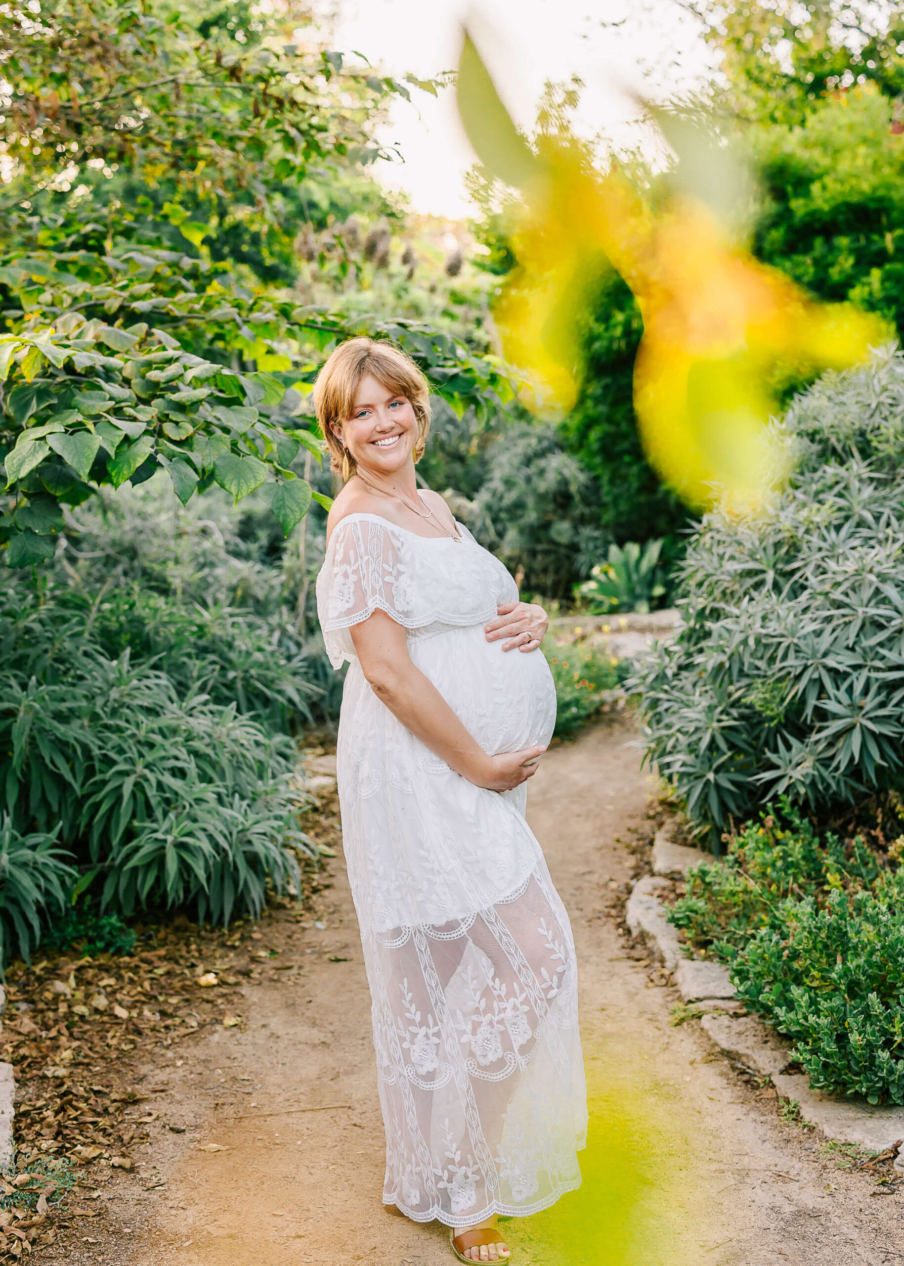Expectant Mama wearing a beautiful boho white lace dress smiling in outdoor nature maternity session.