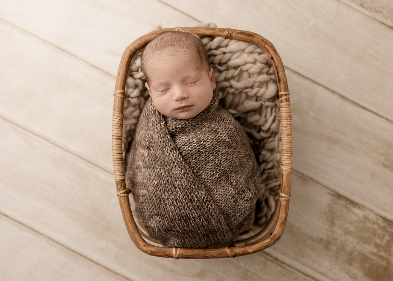 A newborn baby in a brown knit swaddle sleeps in a wicker basket Long Beach Prenatal Yoga