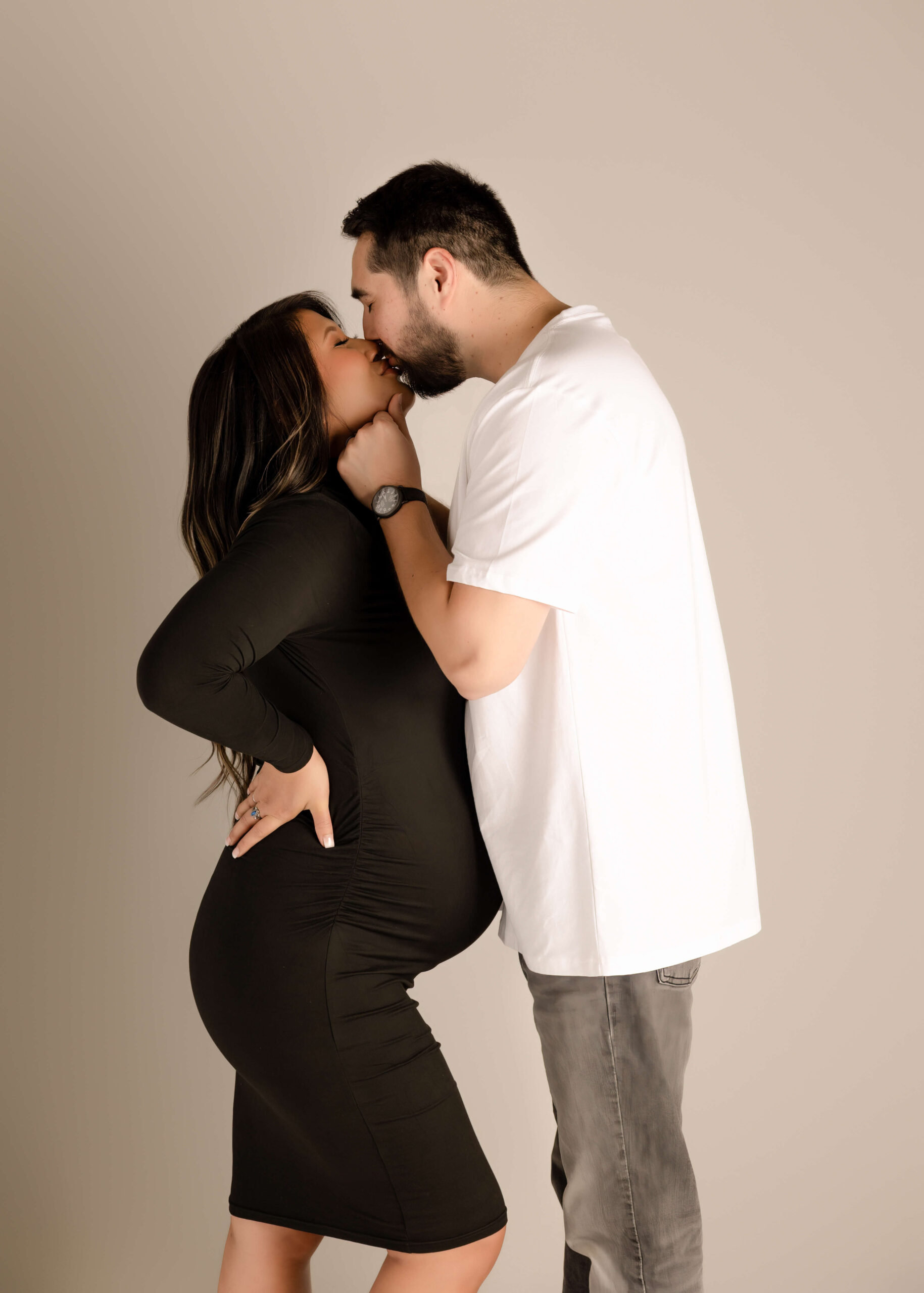 Husband kissing wife while holding her chin at their maternity session.