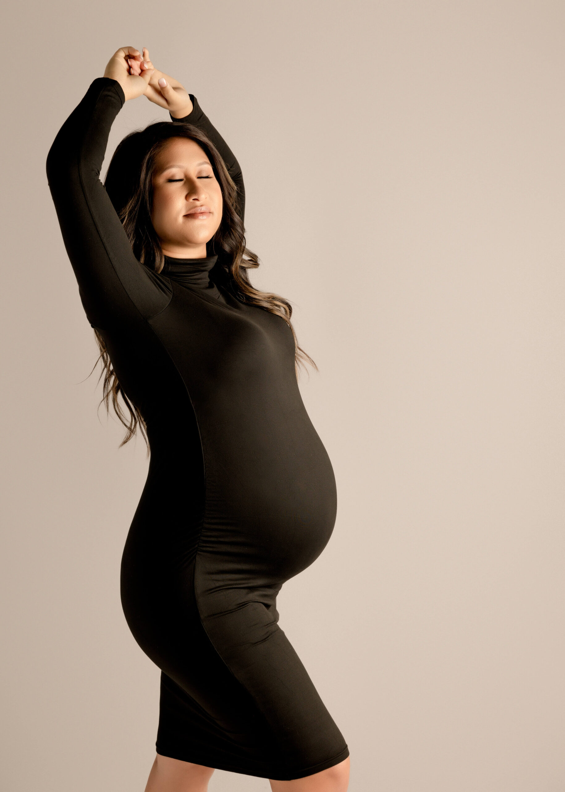 Expectant mom posing in studio with eyes closed for maternity session by Ashley Nicole.