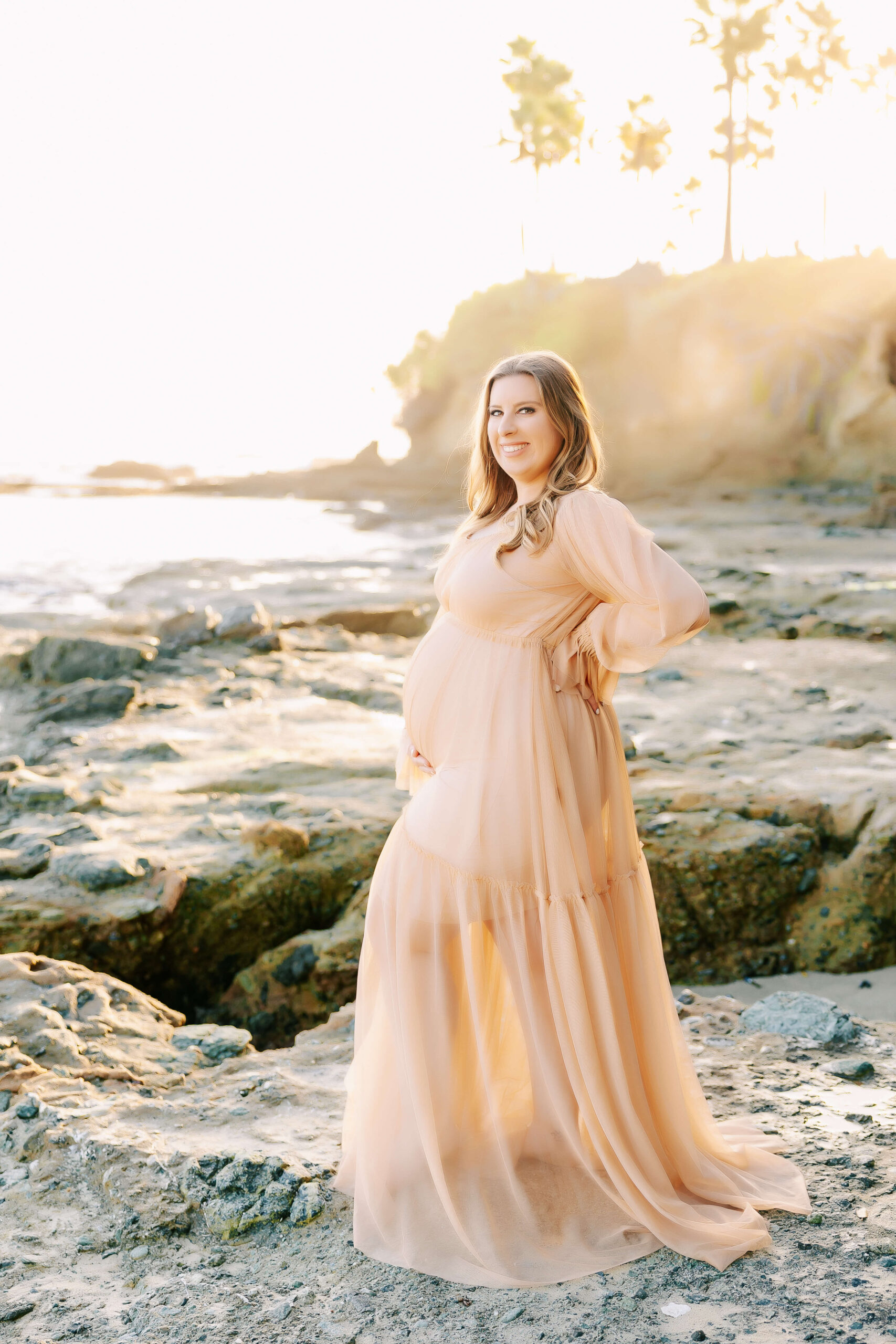 Expectant Mama standing on rocks holding her bump envisioning a water birth in Laguna Beach by Ashley Nicole.