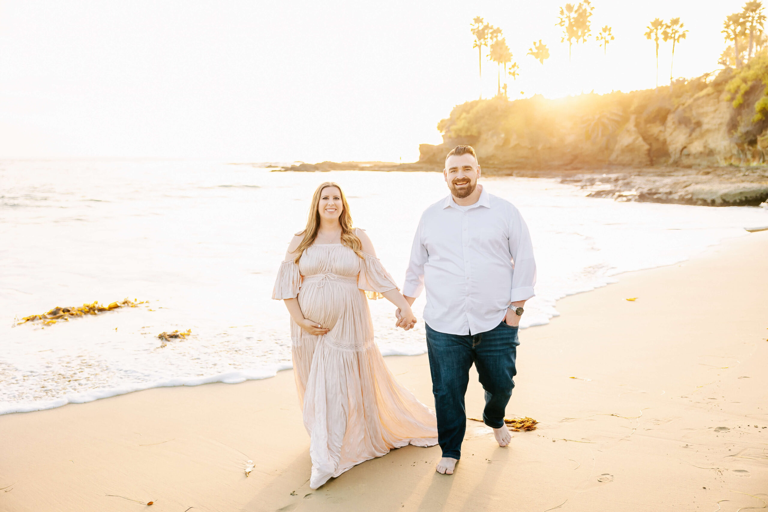 Couple holding hands and walking on beach envision a water birth during maternity session by Ashley Nicole.