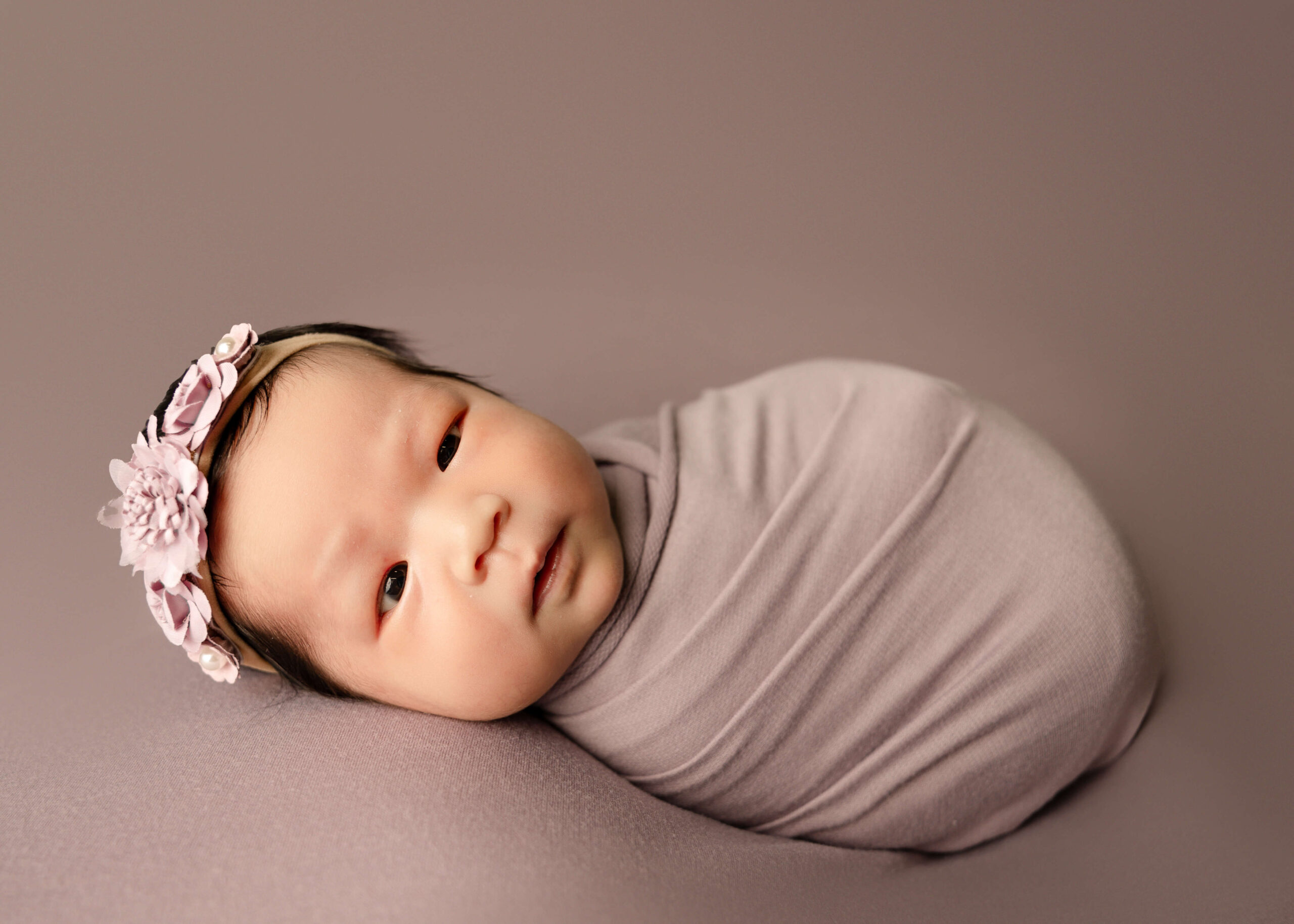 Baby girl wrapped in purple blanket wide awake in Orange County Newborn Studio Session by Ashley Nicole Photography.