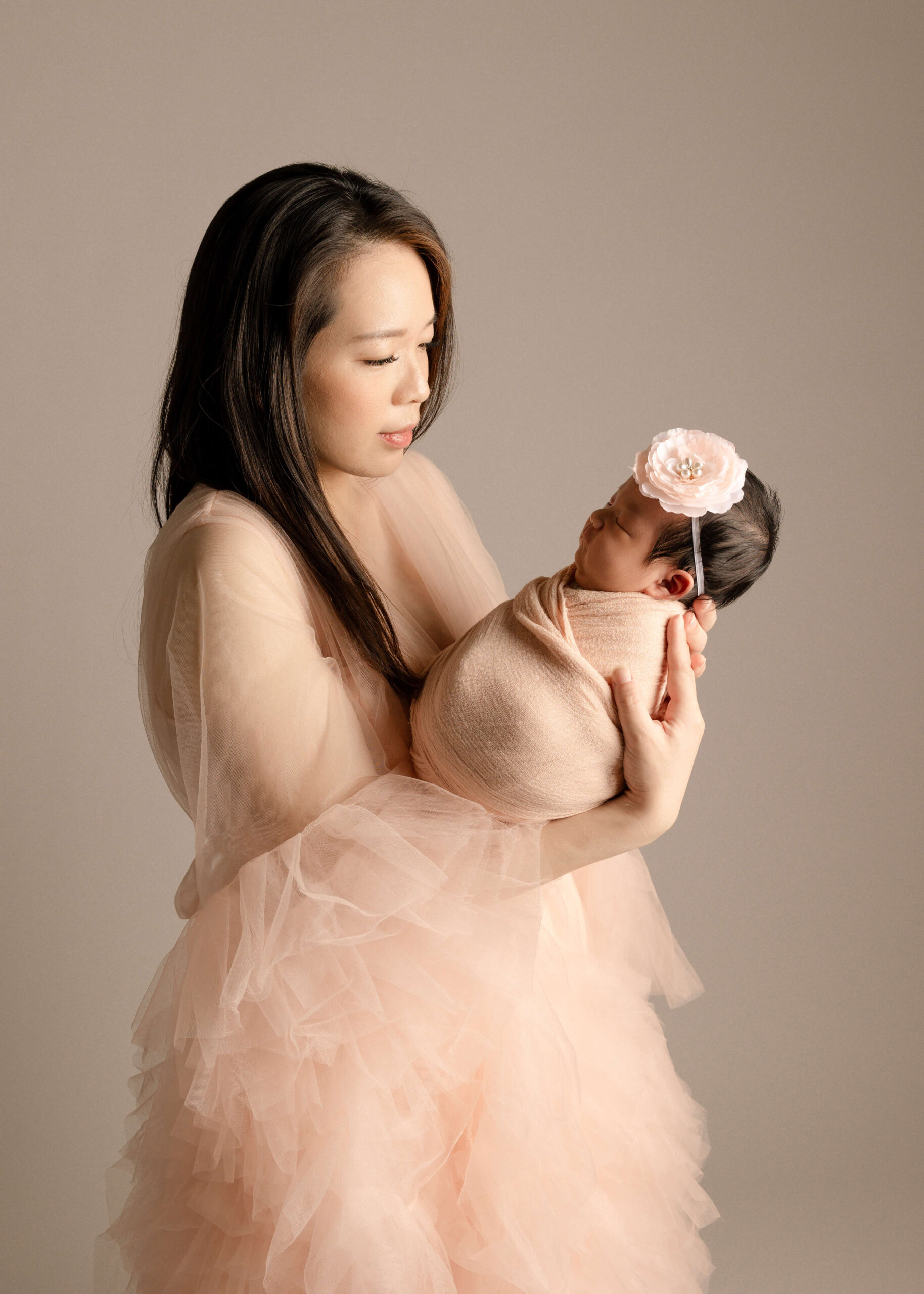 Mom wearing pink ruffled robe holding her baby while looking down at her in Orange County studio by Ashley Nicole.