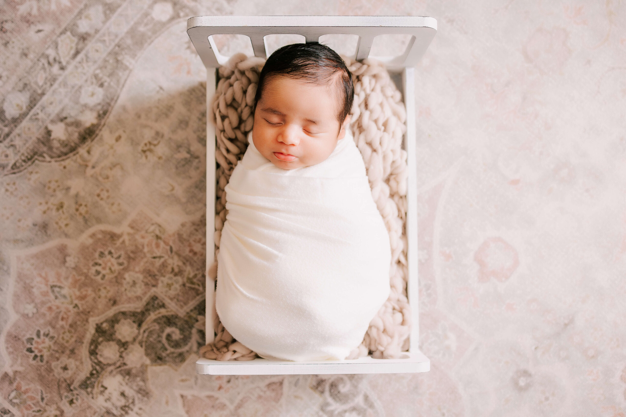 Baby wrapped in white swaddle, posed sleeping in baby prop bed in newborn session in boho studio in Huntington Beach CA by Ashley Nicole. For Postpartum Doula Los Angeles.