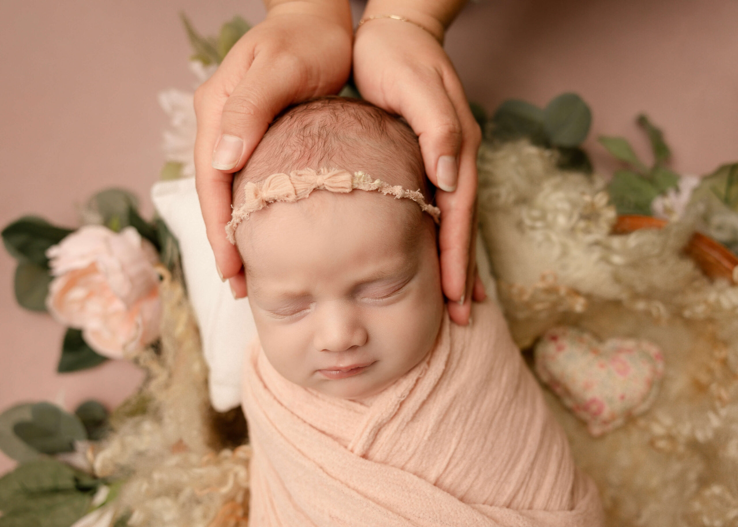 Sleeping baby girl wrapped in pink blanket with mom holding her head in studio by Ashley Nicole.