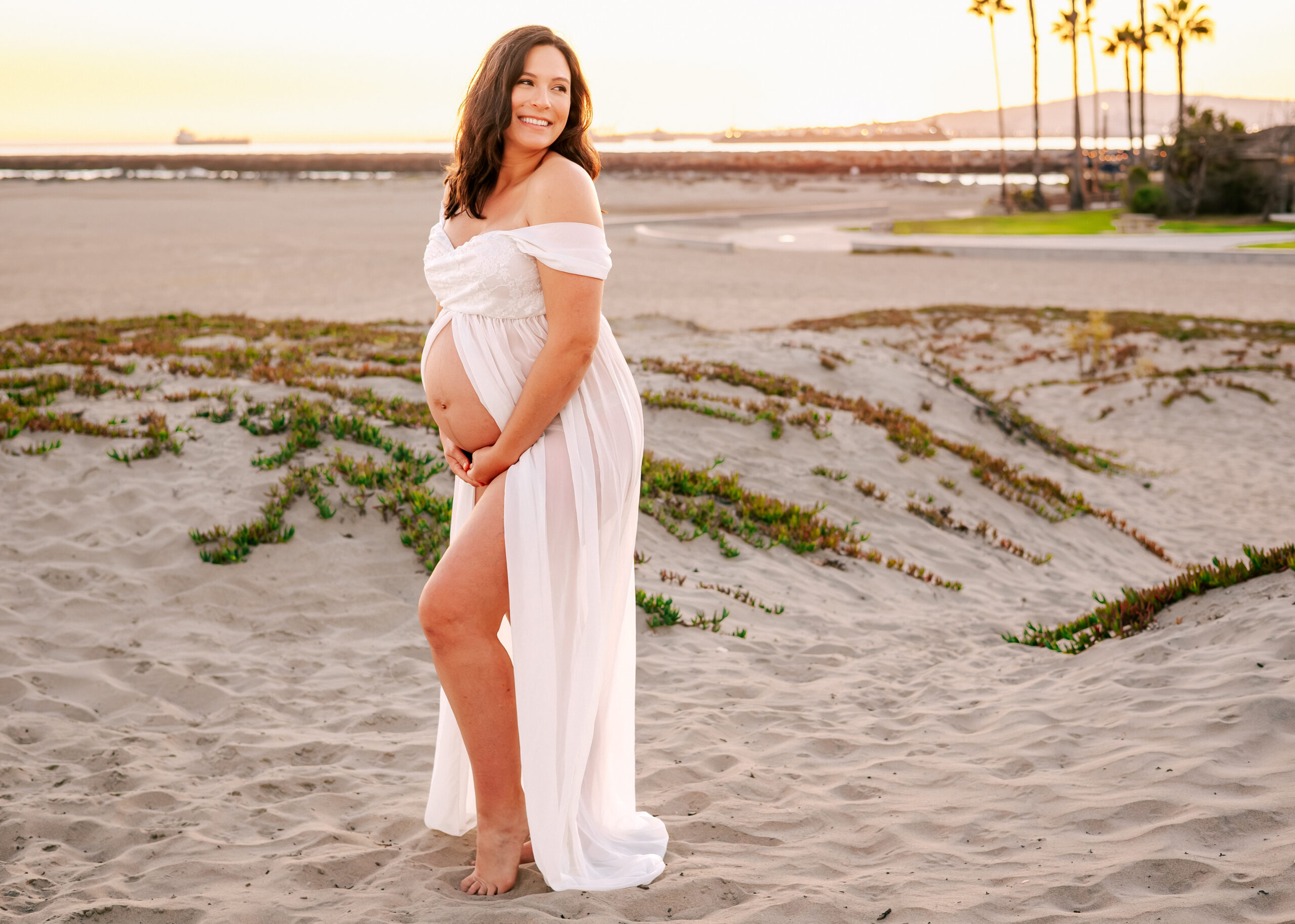 Momma at her maternity shoot wearing white open belly dress at Seal Beach Sand Dunes by Ashley Nicole.