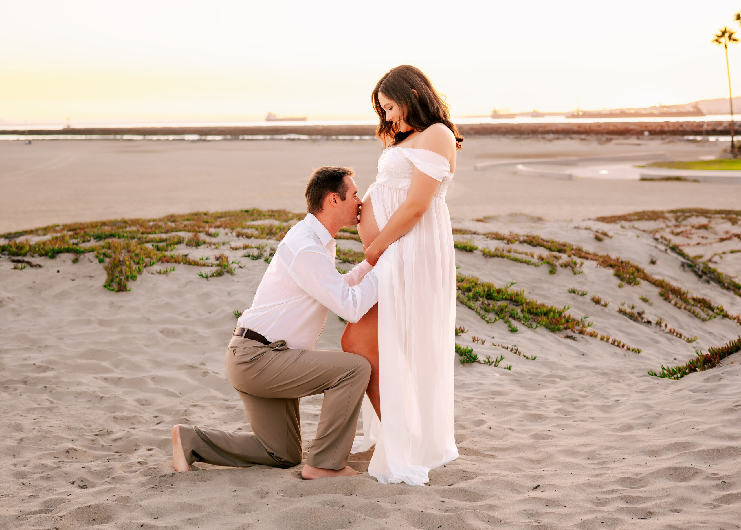 Golden hour maternity session in Seal Beach where husband is kissing wife's belly shot by Ashley Nicole Photography.