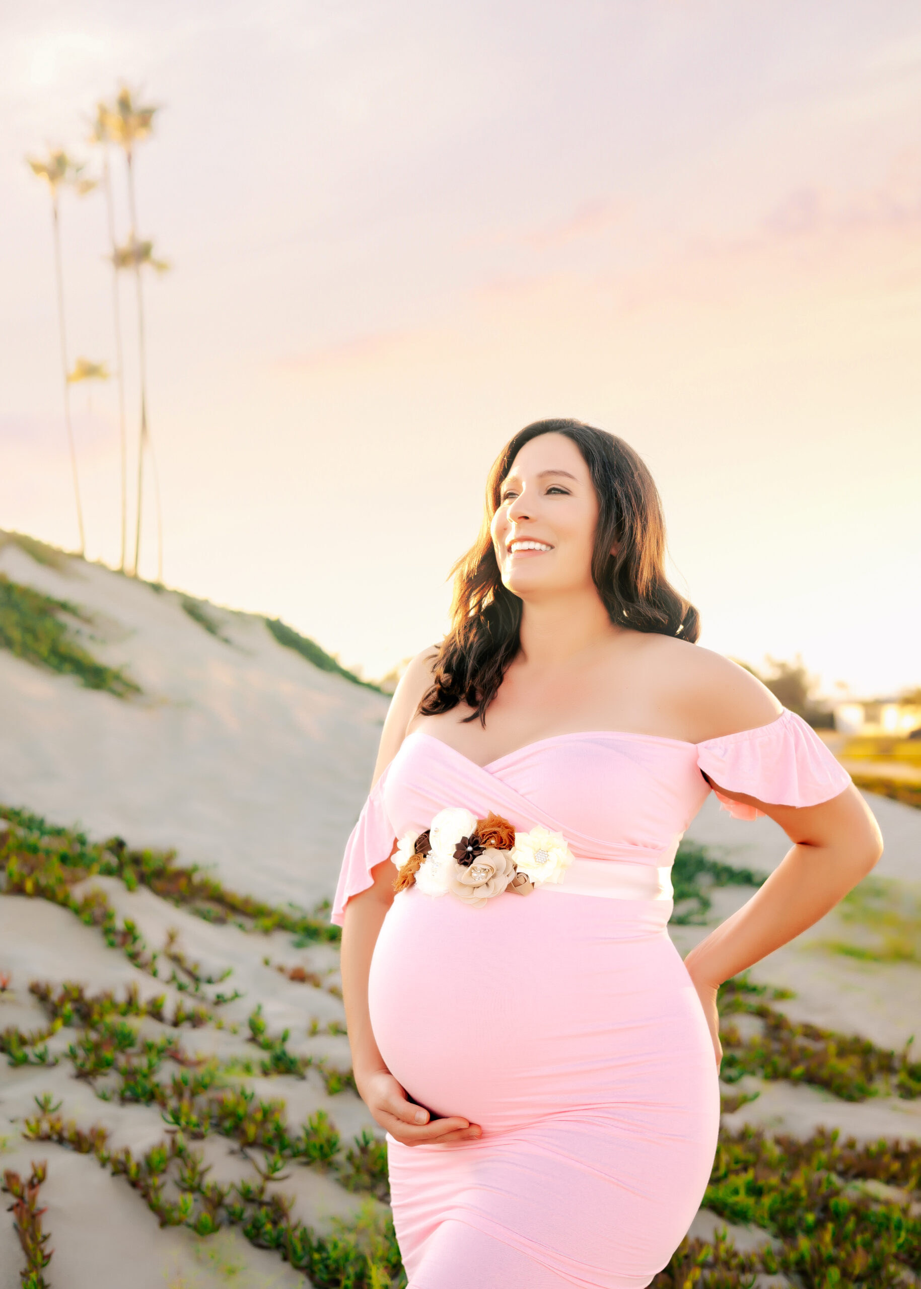 Expectant Mama gazing off in the distance holding her baby bump during golden hour beach maternity session Seal Beach, CA by Ashley Nicole.