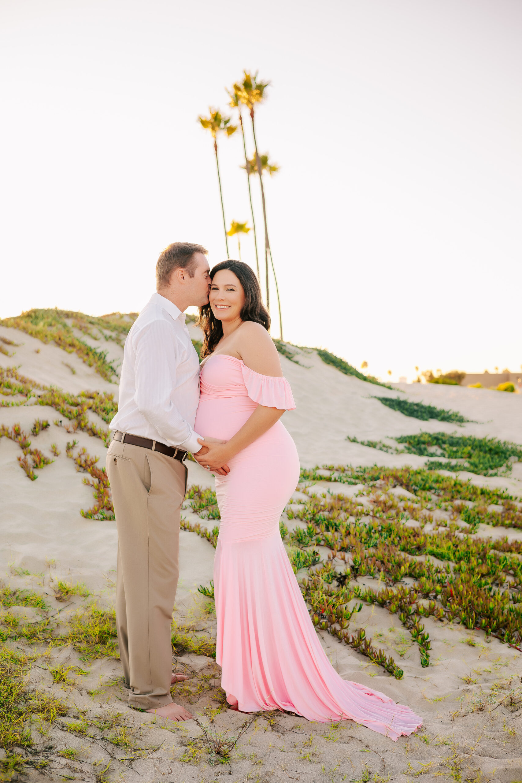 Husband kissing side of wife's head during maternity session in Seal Beach, CA by Ashley Nicole Photography.
