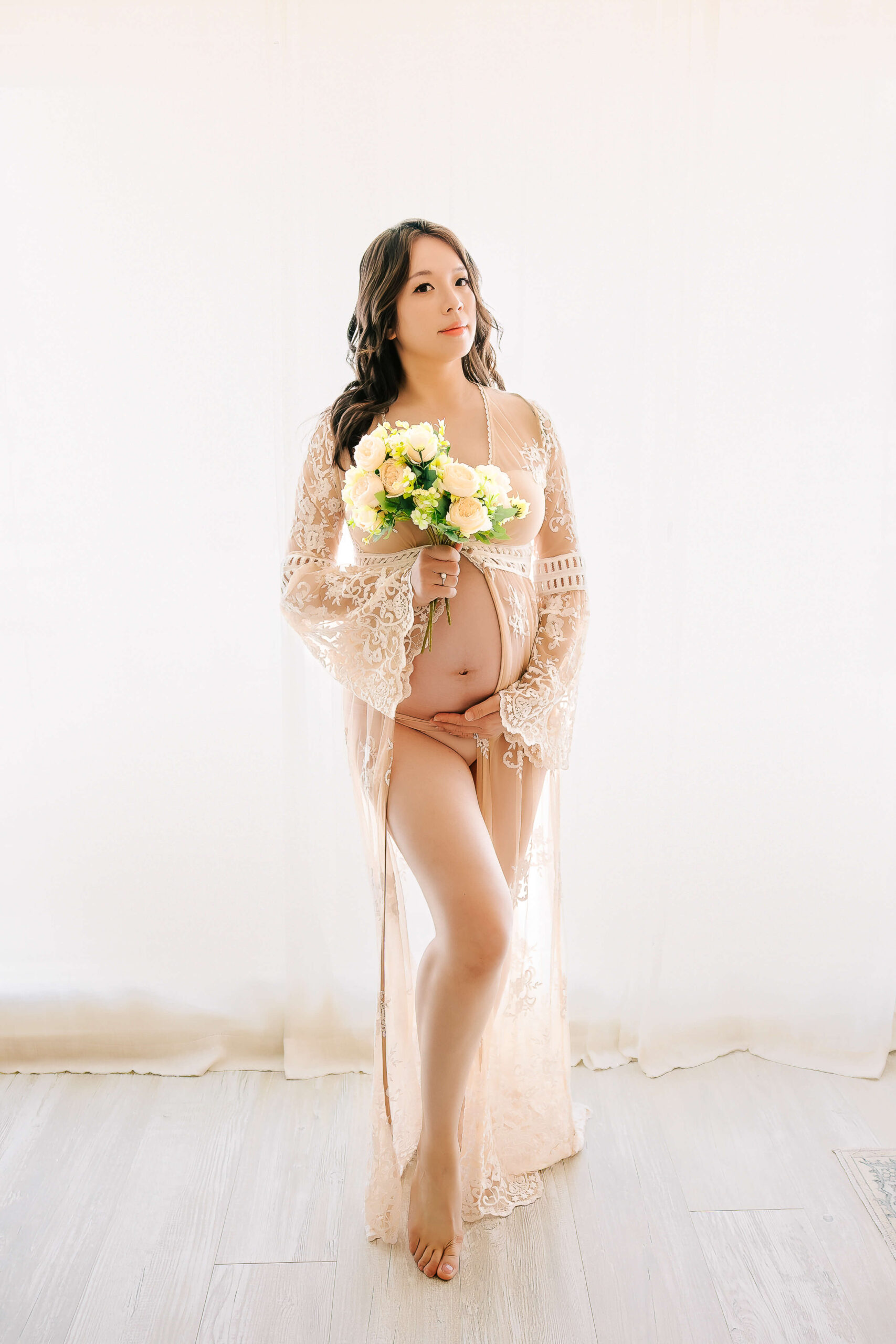 Expectant mom wear kimono robe holding flowers in her maternity boudoir session in studio in Huntington Beach, CA by Ashley Nicole Photography.