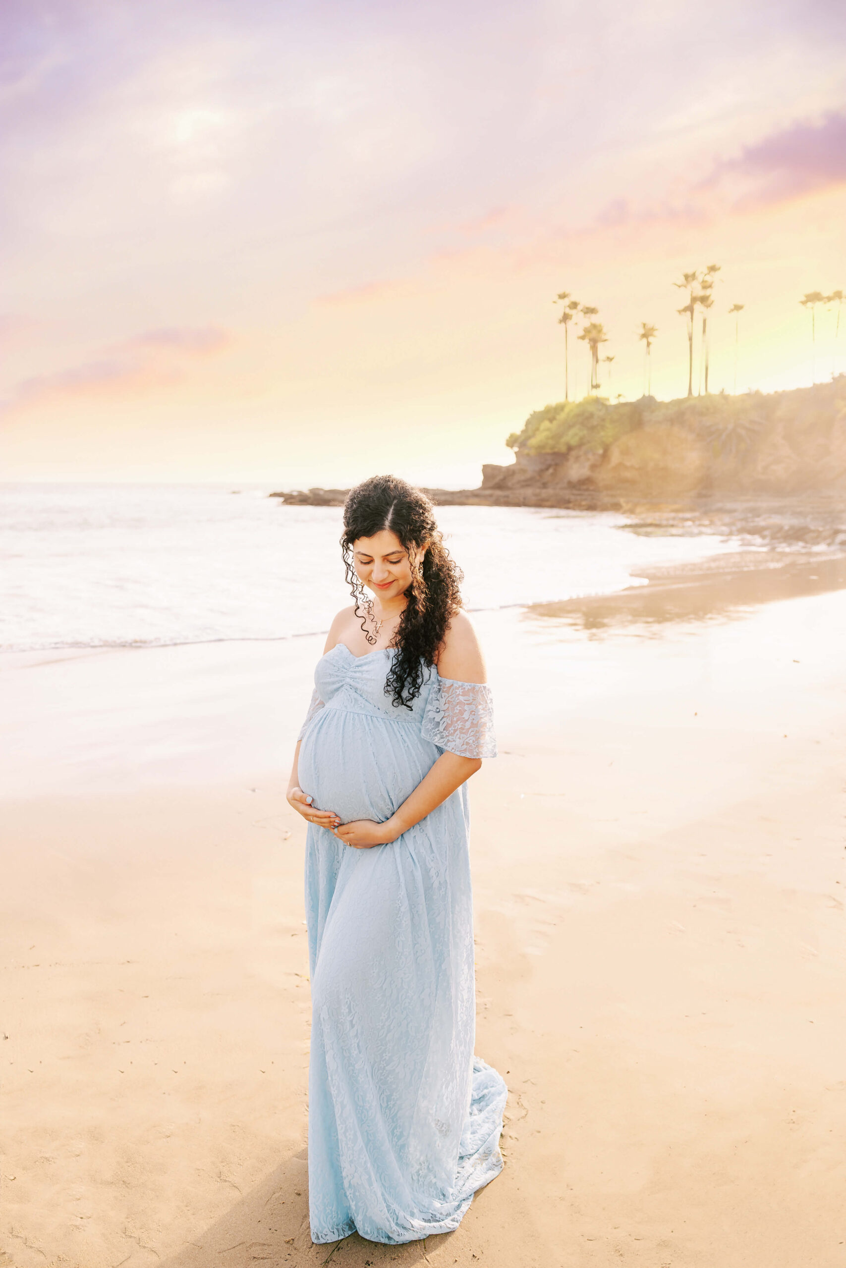 Pregnant mom holding belly looking down with eyes closed dreaming of her baby during maternity session in Laguna Beach, Ca by Ashley Nicole.