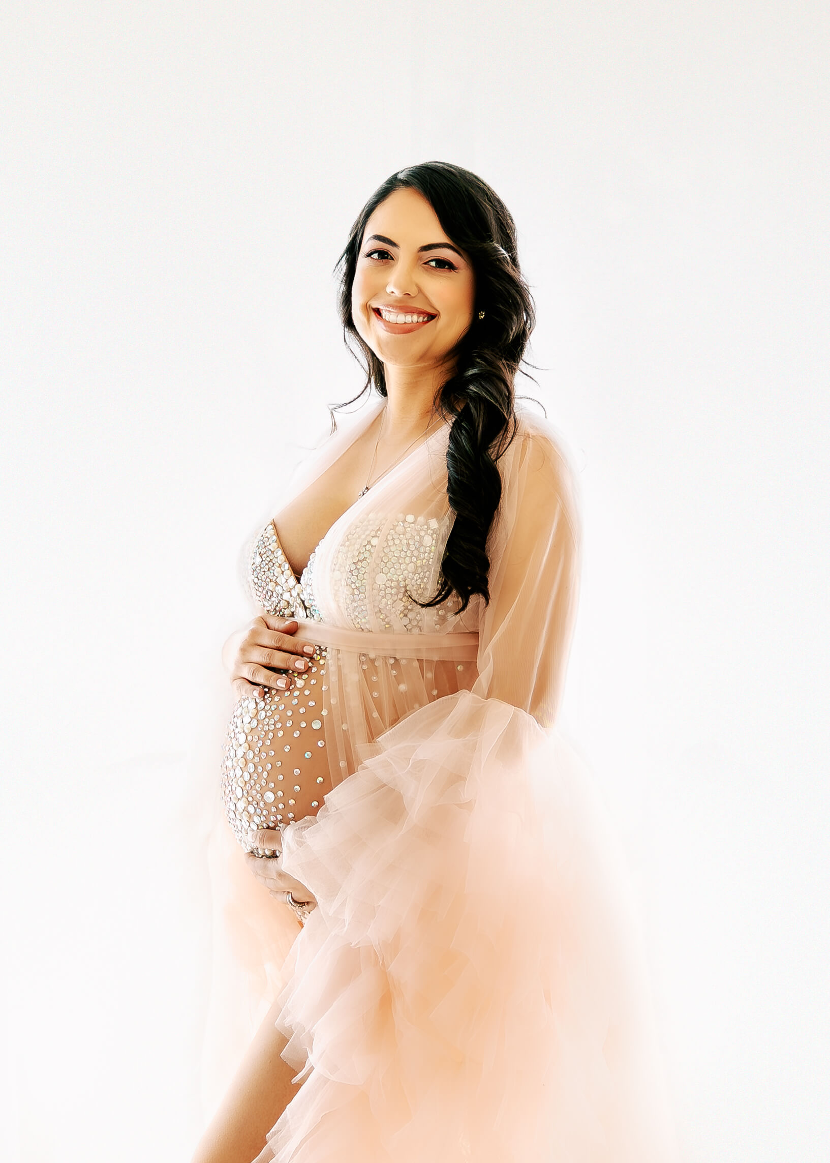 Gorgeous expectant Mama posed smiling and wearing jeweled bodysuit and ruffled robe by Ashley Nicole.
