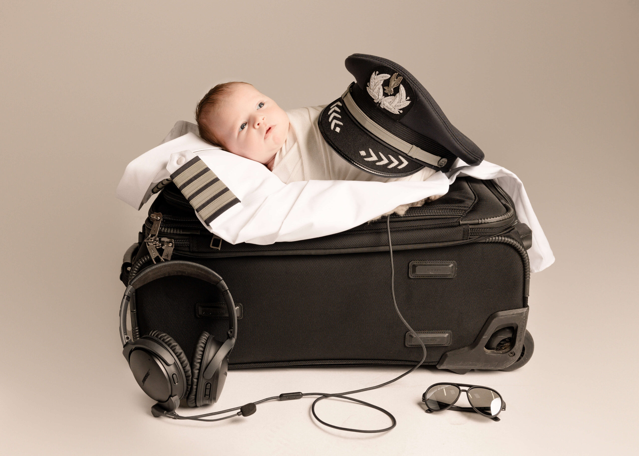 Baby posed on pilot dads suitcase with pilot shirt and hat in studio in Orange County, CA by Ashley Nicole.