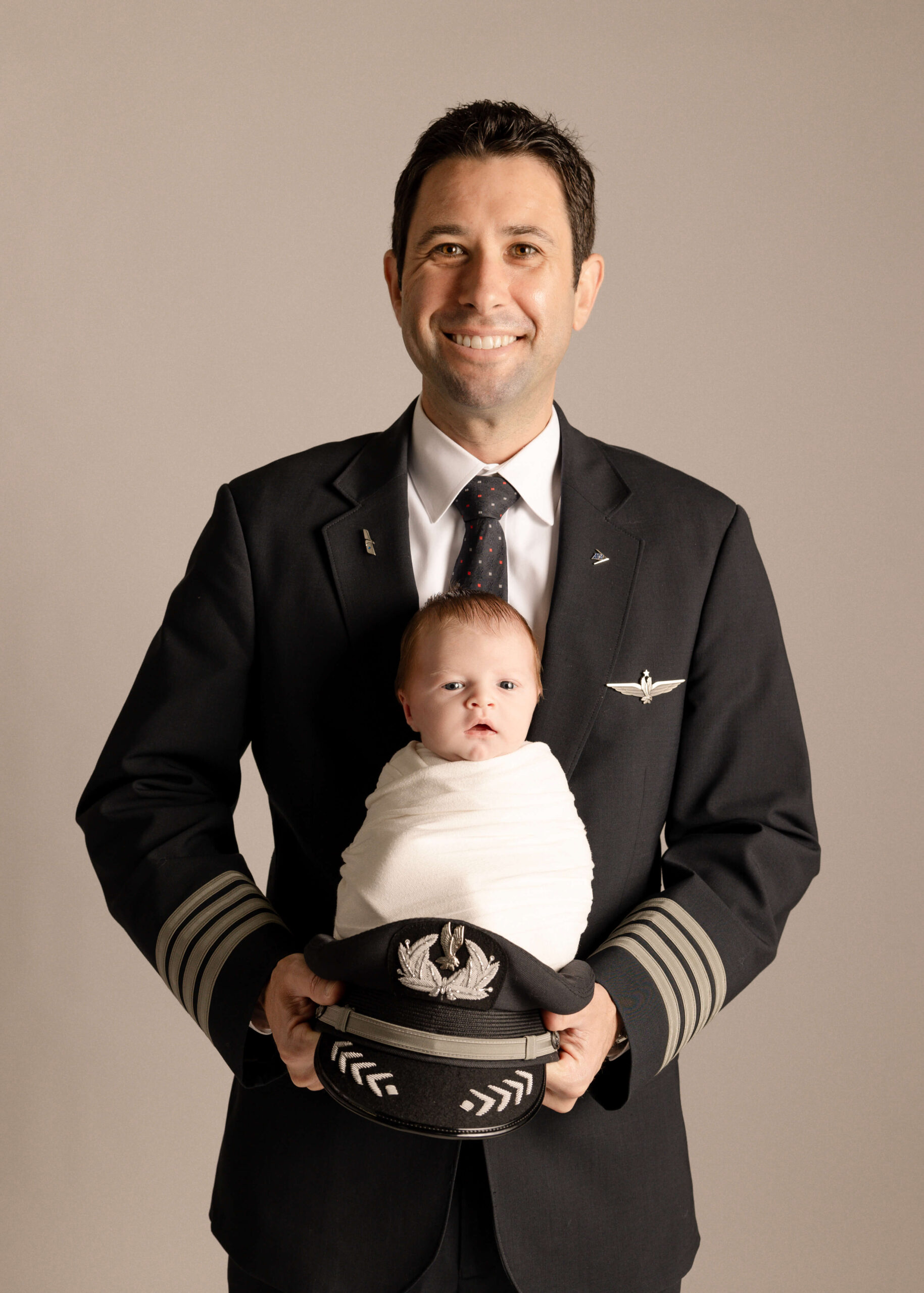 Pilot dad wearing uniform hiding baby infant of him on hat in studio in Orange County, CA by Ashley Nicole..