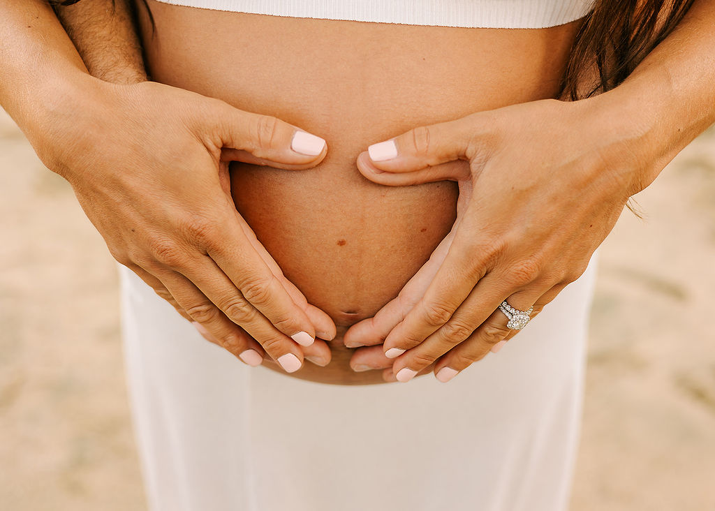 Details of expecting parents holding the bump with hands in the shape of a heart