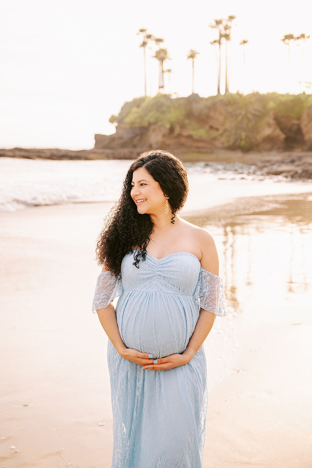 A happy mom to be in a lace blue maternity dress walking on the beach at sunset after meeting a Doula in Long Beach