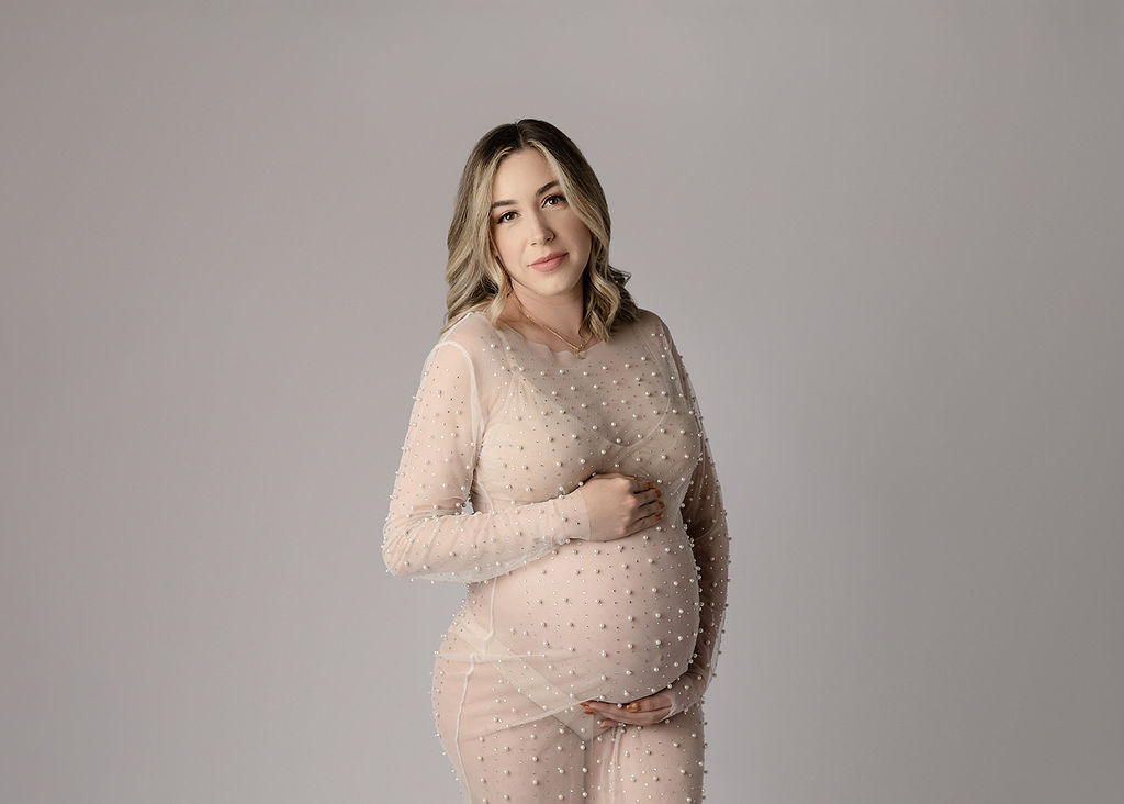 A mother to be in a pearl studded sheer maternity coverup holds her bump while walking in a studio