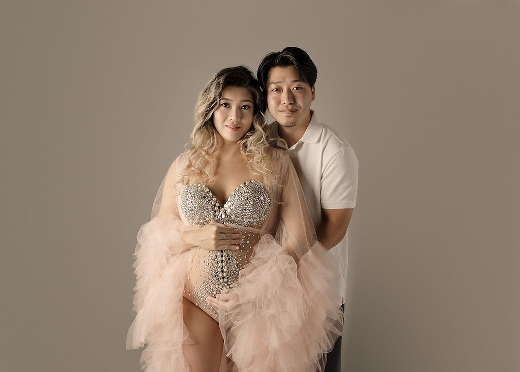 Happy expecting parents stand in a studio holding the bump and smiling