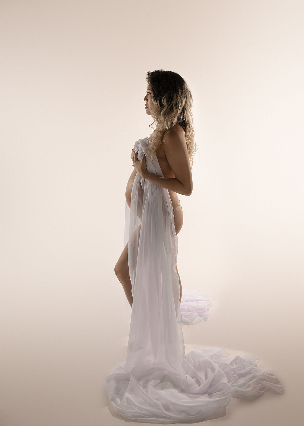 A mom to be stands in a studio covering with a white sheet after meeting a Long Beach OBGYN